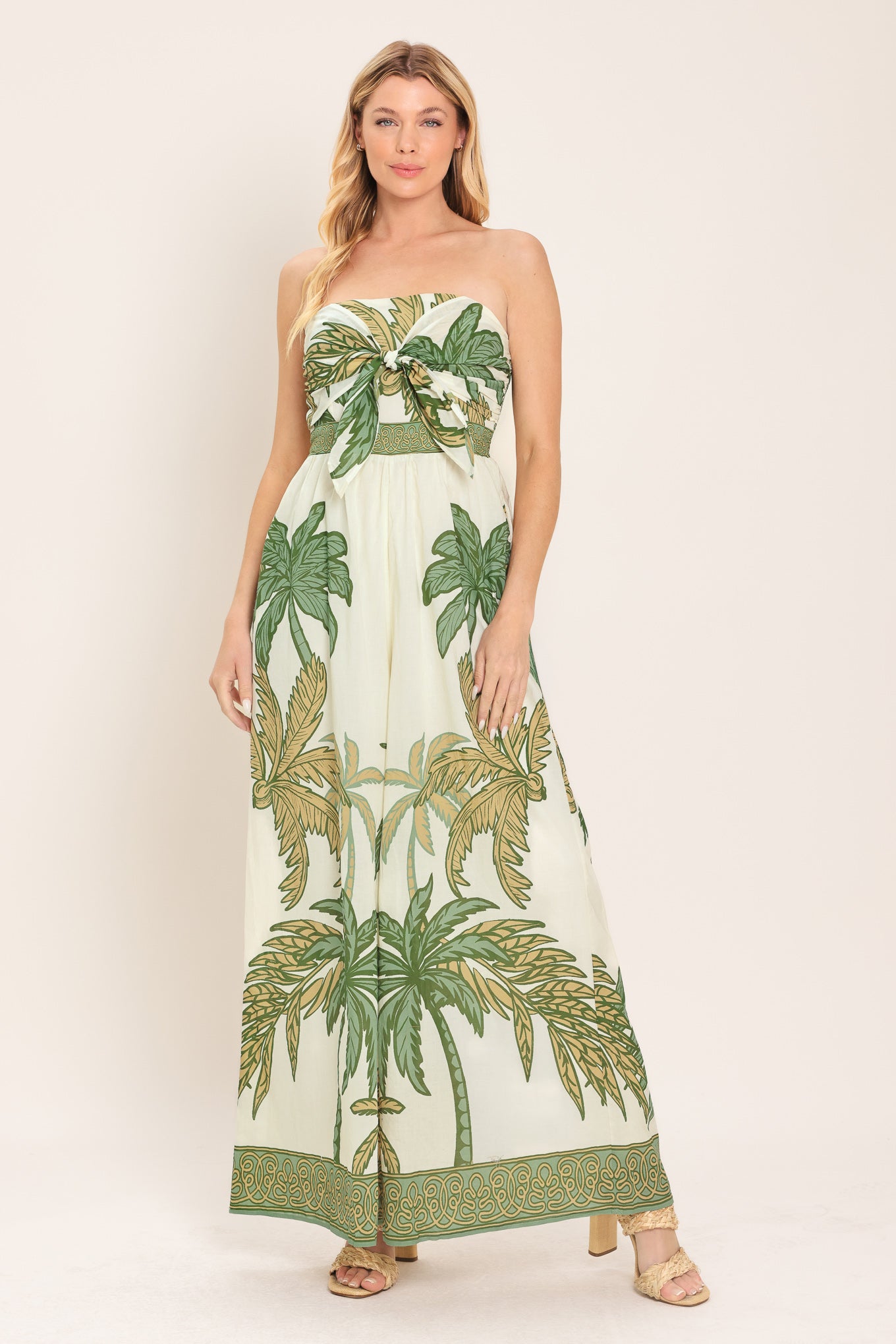 Woman wearing a strapless wide-leg jumpsuit with palm tree pattern featuring front tie and smocked back bodice | Flying Tomato