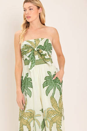 Woman wearing a strapless ivory wide-leg jumpsuit with green palm tree pattern featuring front tie and smocked back bodice | Flying Tomato