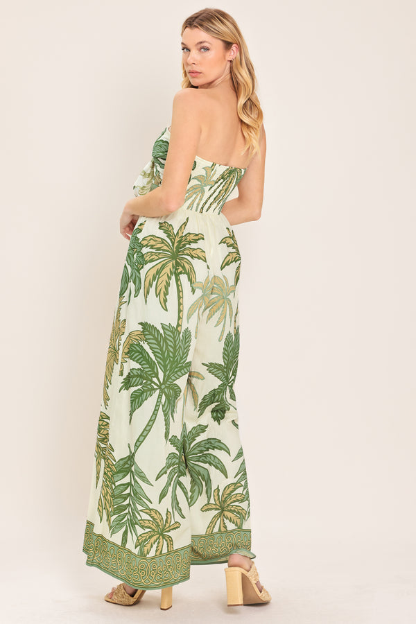 Woman wearing a strapless ivory wide-leg jumpsuit with green palm tree pattern featuring front tie and smocked back bodice | Flying Tomato