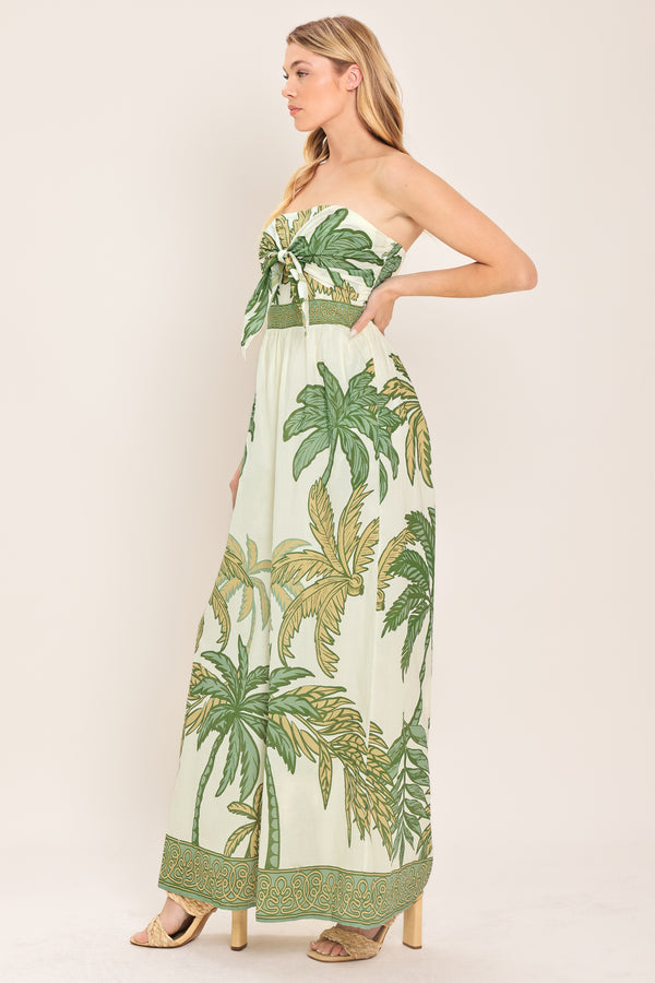 Woman wearing a strapless ivory wide-leg jumpsuit with green palm tree pattern featuring front tie and smocked back bodice | Flying Tomato