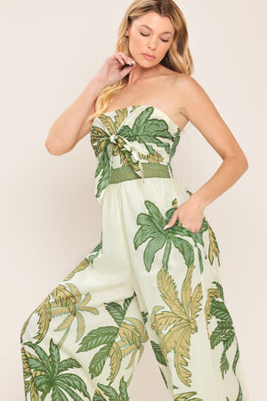 Woman wearing a strapless ivory wide-leg jumpsuit with green palm tree pattern featuring front tie and smocked back bodice | Flying Tomato