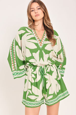Woman wearing a green and white leaf pattern romper featuring V neckline, kimono sleeve, elastic waist with tie tassel and back neck button closure | Flying Tomato