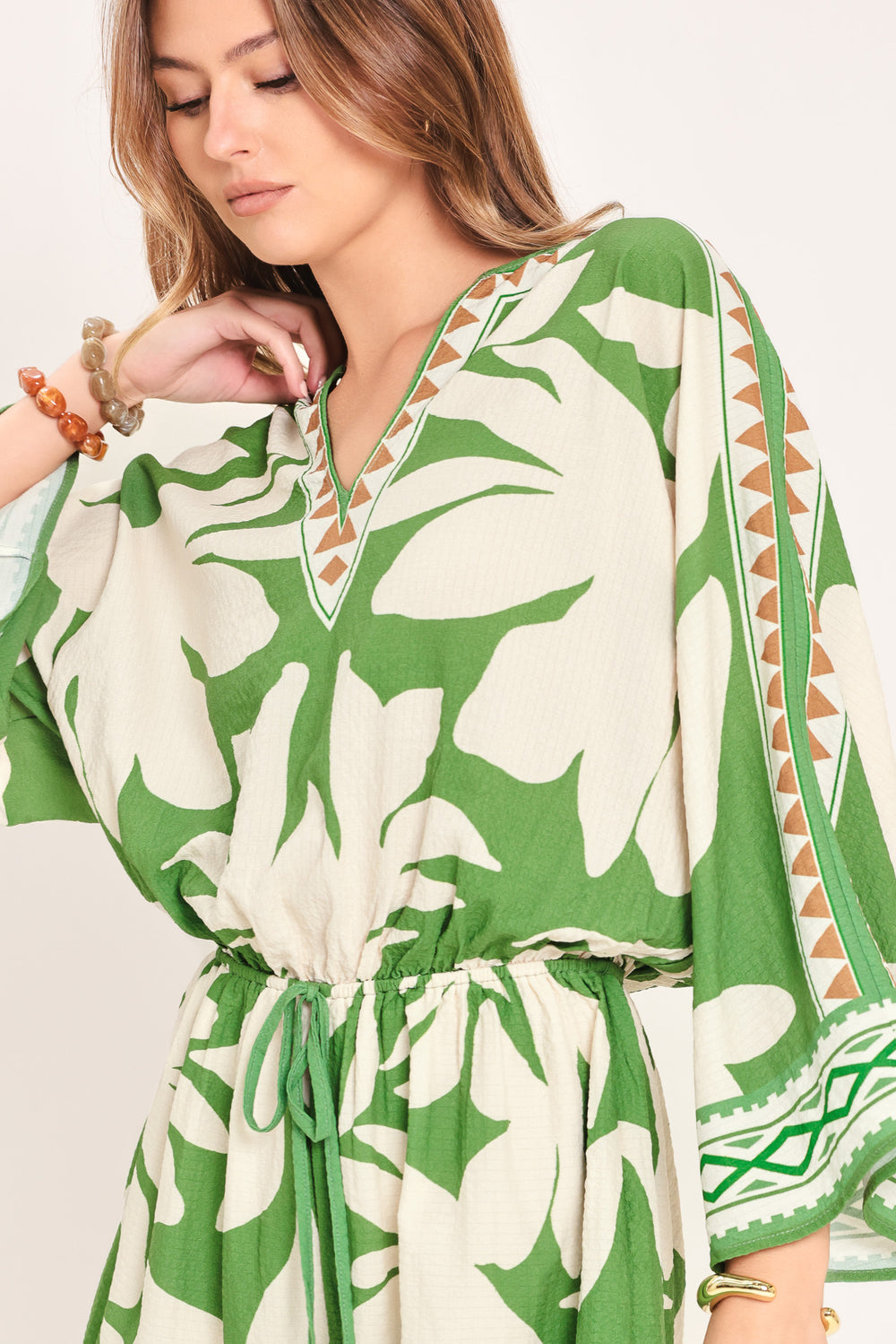 Woman wearing a green and white leaf pattern romper featuring V neckline, kimono sleeve, elastic waist with tie tassel and back neck button closure | Flying Tomato