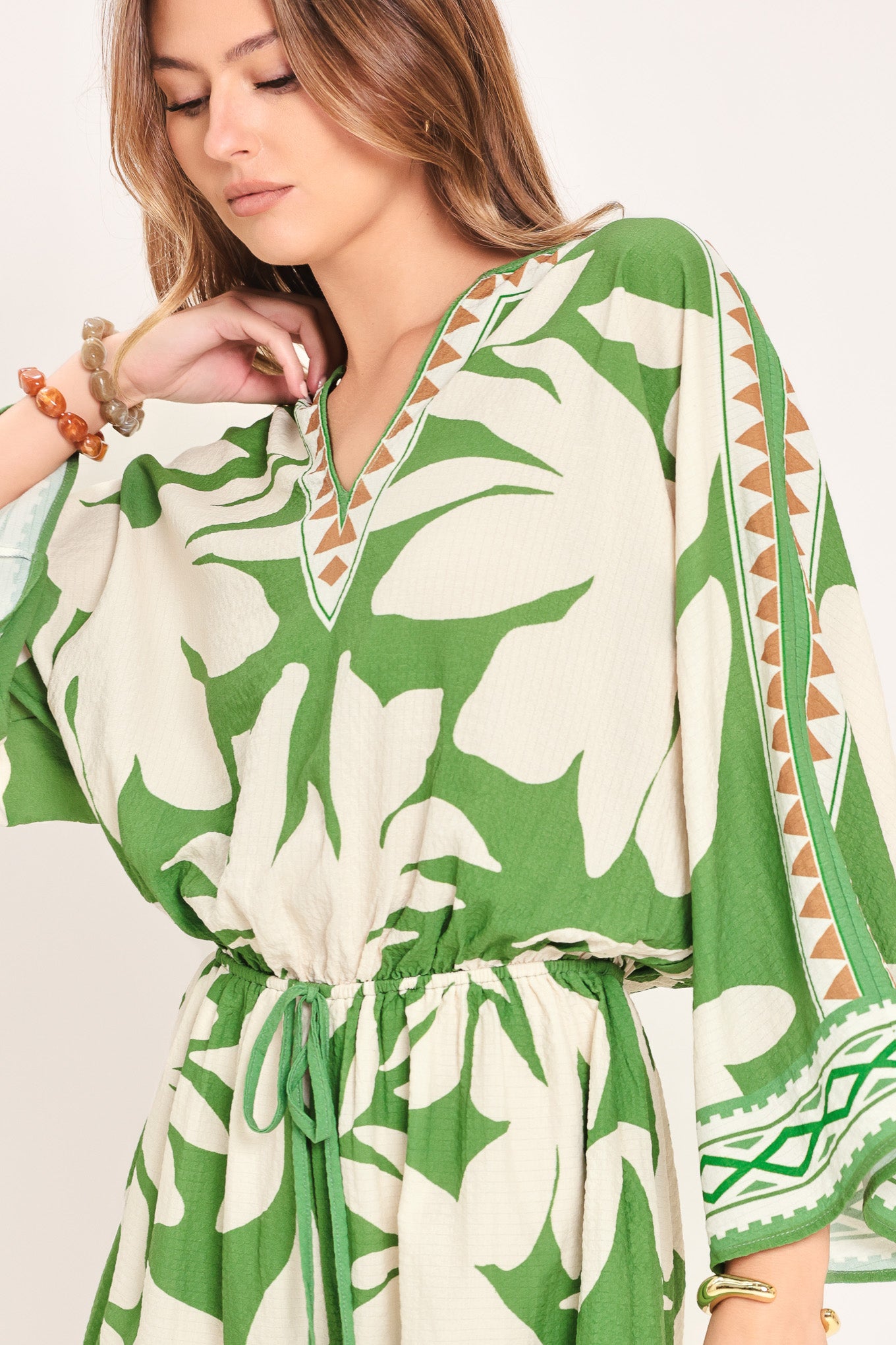 Woman wearing a green and white leaf pattern romper featuring V neckline, kimono sleeve, elastic waist with tie tassel and back neck button closure | Flying Tomato