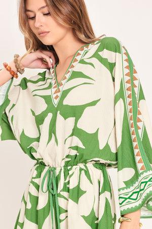 Woman wearing a green and white leaf pattern romper featuring V neckline, kimono sleeve, elastic waist with tie tassel and back neck button closure | Flying Tomato