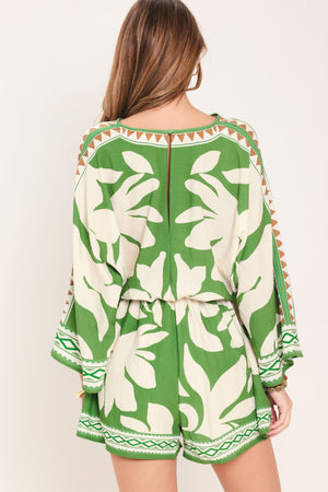 Woman wearing a green and white leaf pattern romper featuring V neckline, kimono sleeve, elastic waist with tie tassel and back neck button closure | Flying Tomato