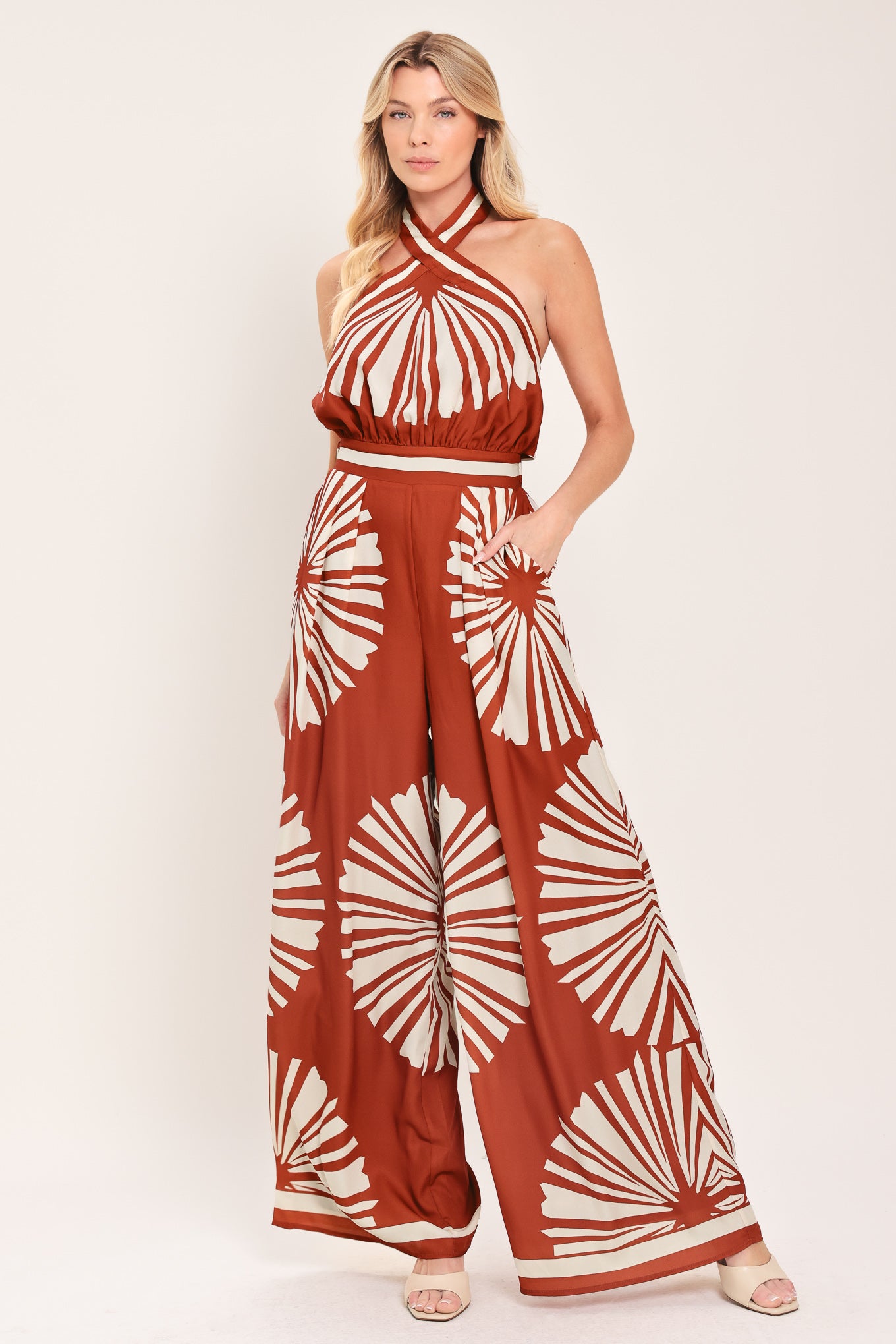 Woman wearing a terracotta wide leg jumpsuit with beige circular print featuring halter neckline with twist strap and back button closure, and bare back with tie closure | Flying Tomato