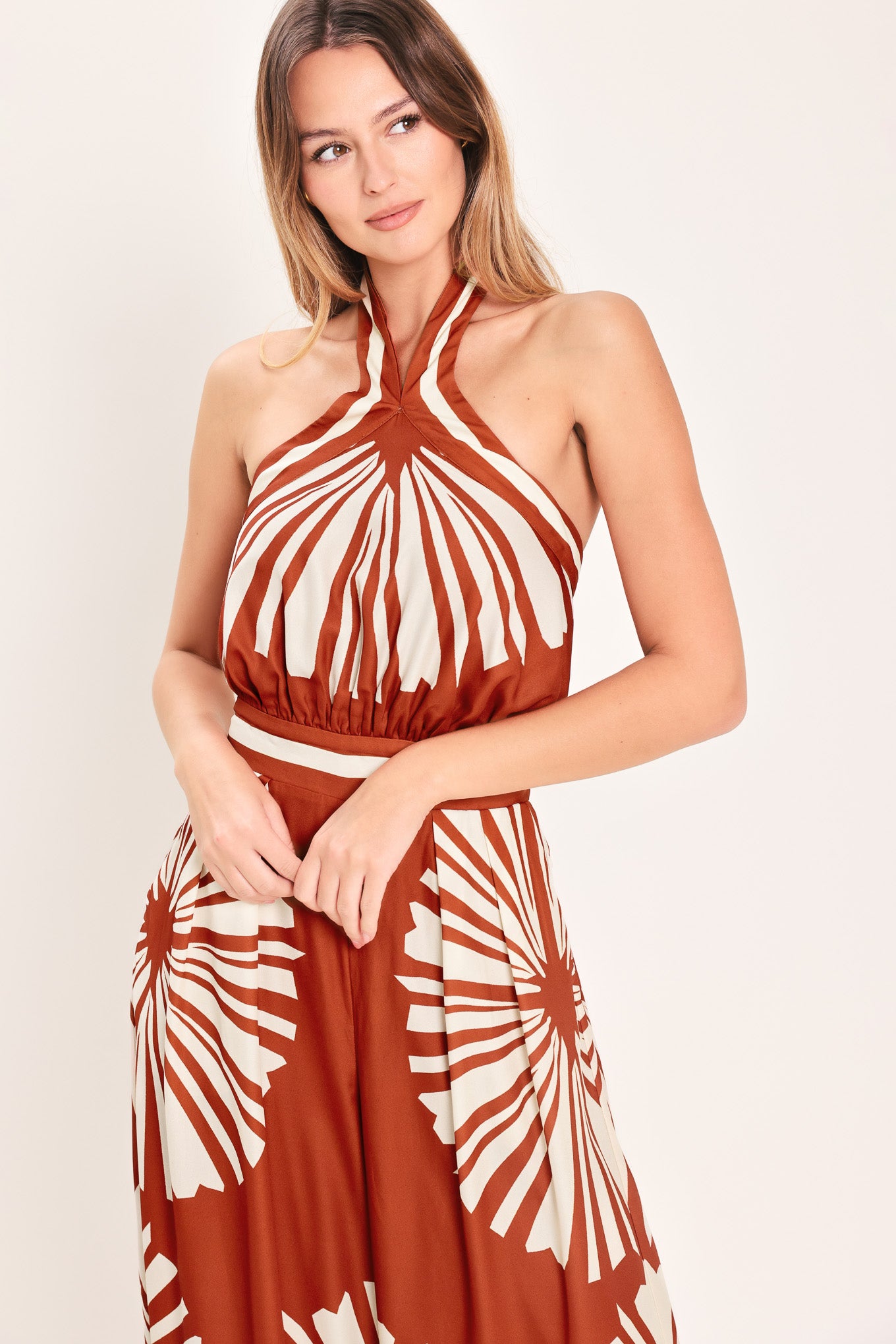 Woman wearing a terracotta wide leg jumpsuit with beige circular print featuring halter neckline with twist strap and back button closure, and bare back with tie closure | Flying Tomato