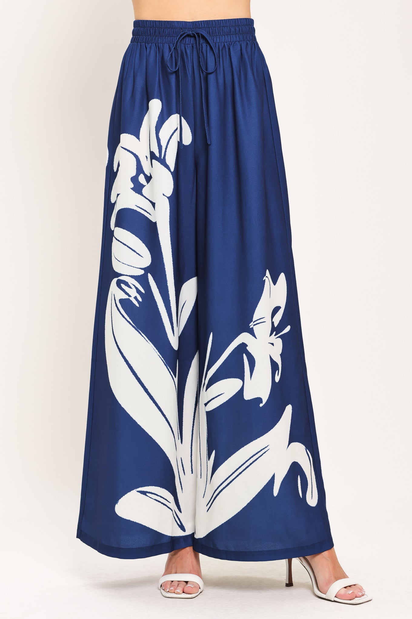 Woman wearing a navy blue with white floral print wide leg pant featuring an elastic waist with tie | Flying Tomato