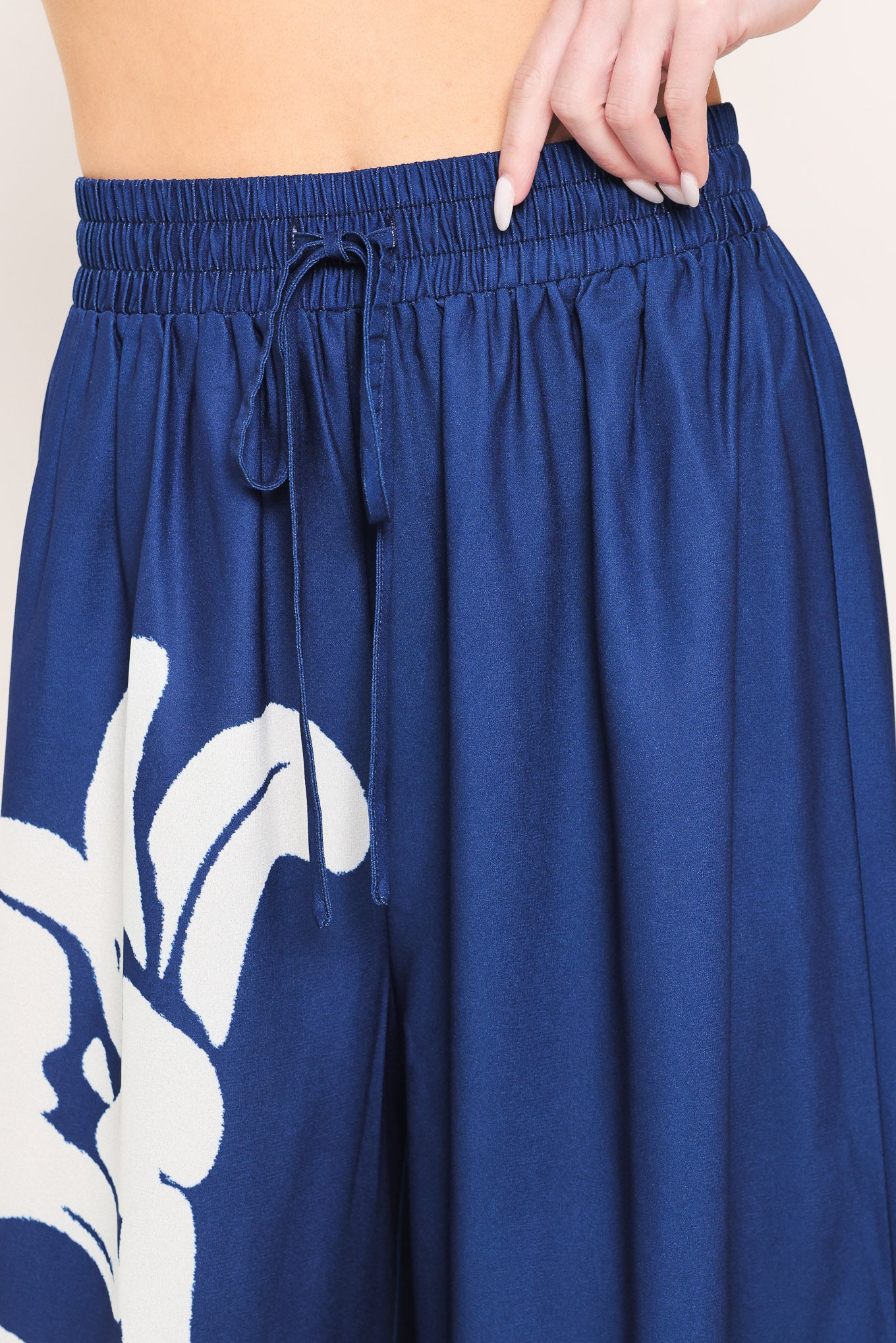 Woman wearing a navy blue with white floral print wide leg pant featuring an elastic waist with tie | Flying Tomato