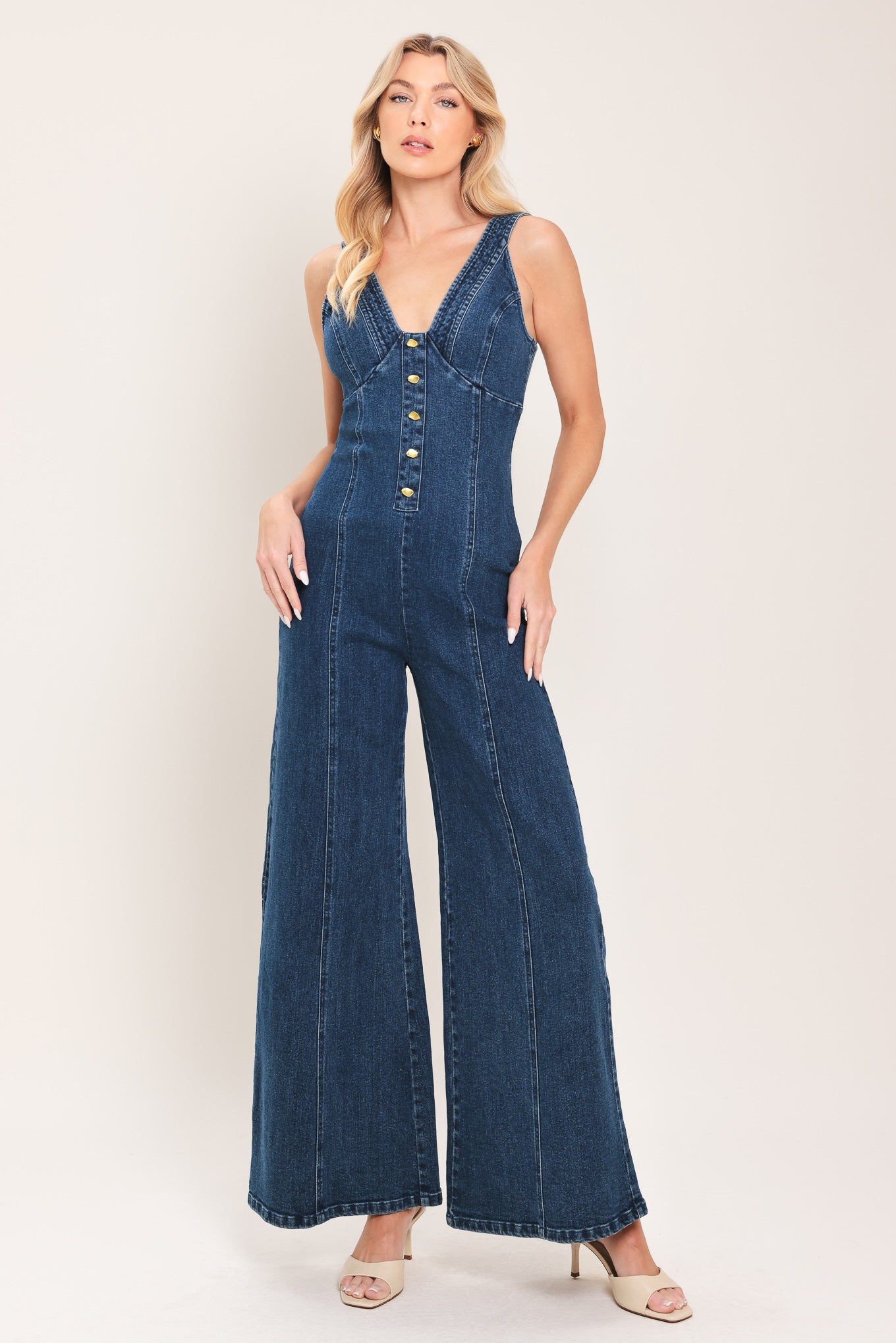Woman wearing a denim jumpsuit featuring V neckline, front button detail, flare leg and smocked back with zipper closure | Flying Tomato