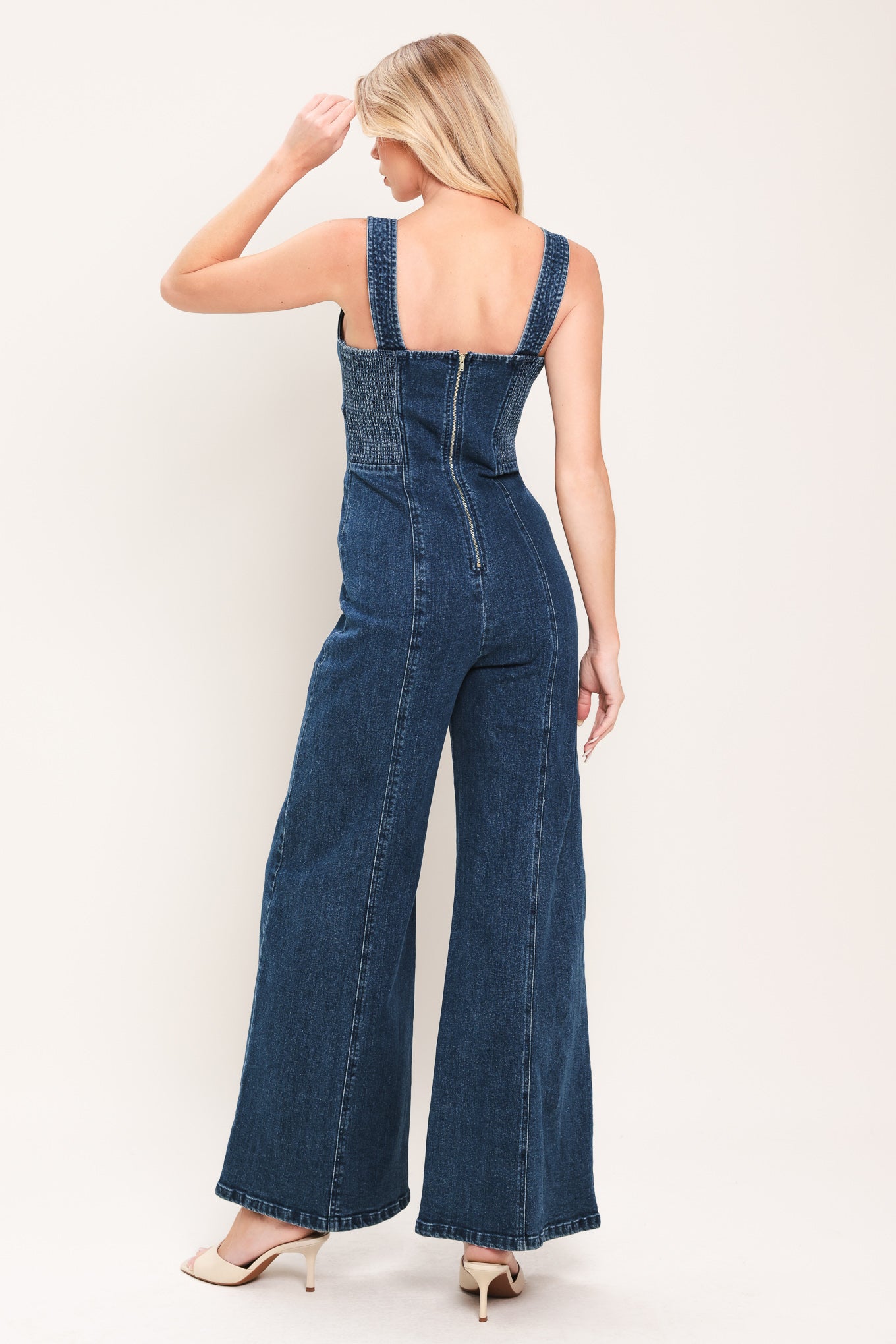Woman wearing a denim jumpsuit featuring V neckline, front button detail, flare leg and smocked back with zipper closure | Flying Tomato