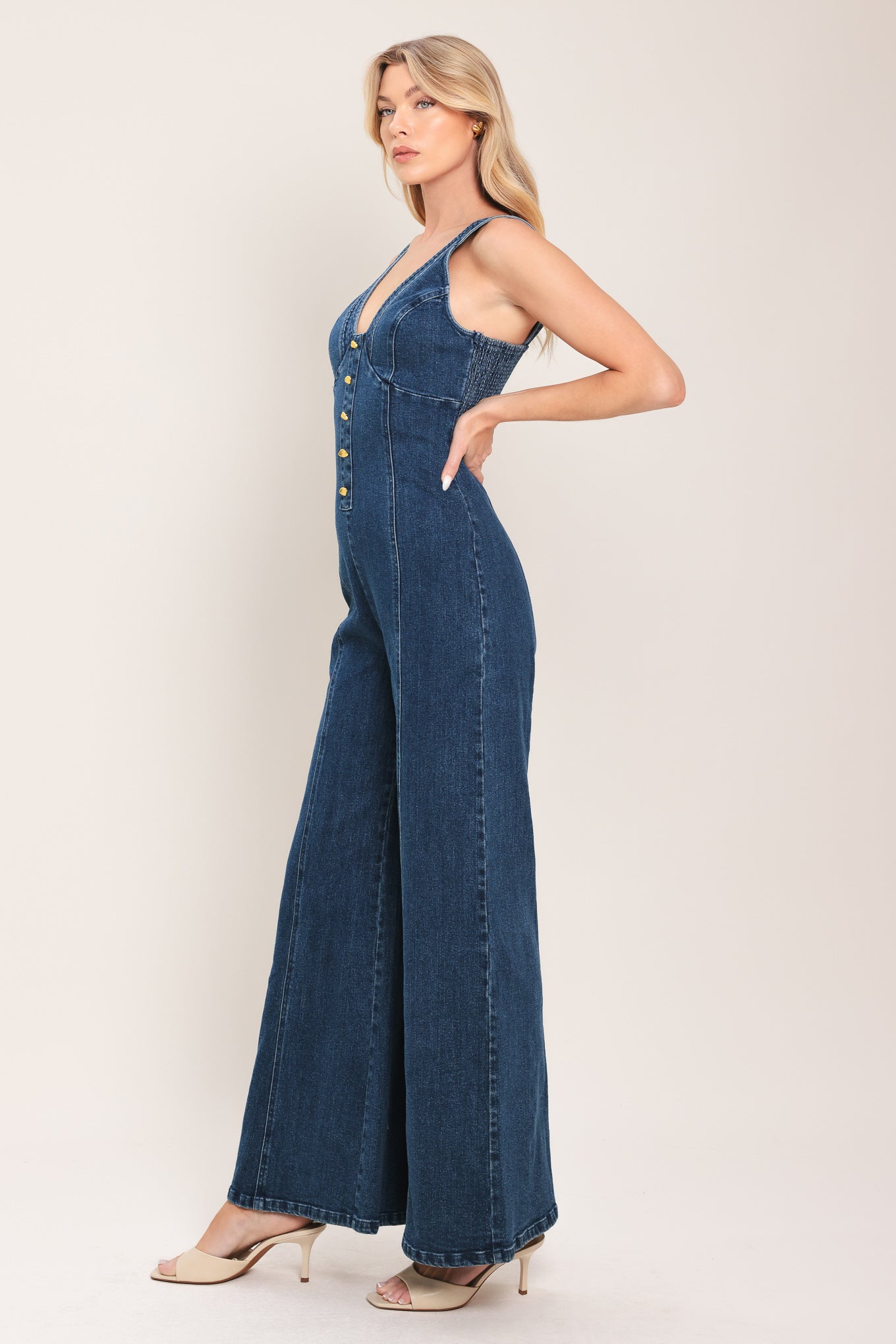 Woman wearing a denim jumpsuit featuring V neckline, front button detail, flare leg and smocked back with zipper closure | Flying Tomato