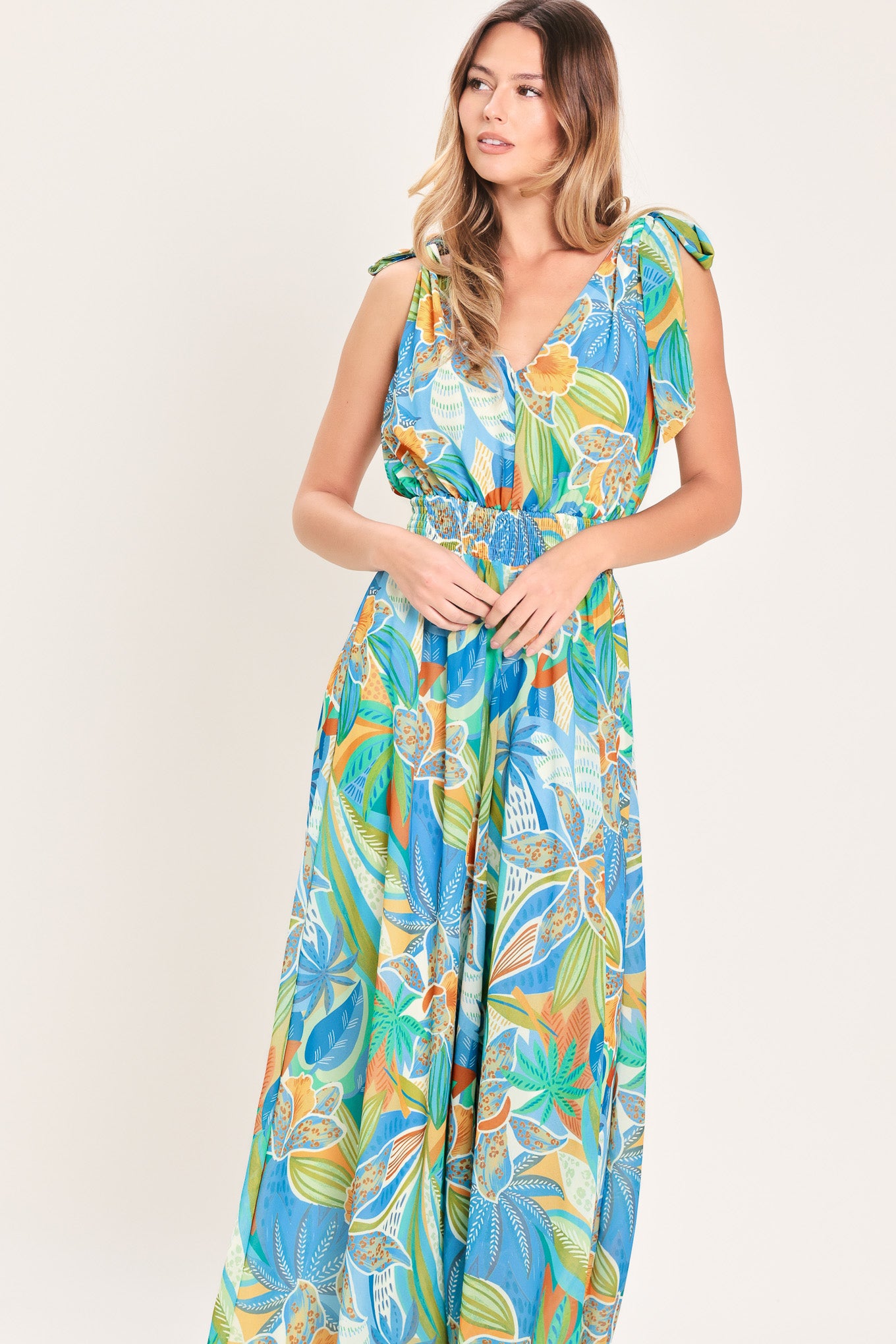 Woman wearing a blue multicolored patterned woven jumpsuit featuring V neckline, shoulder ties, smocked waistband and wide leg | Flying Tomato