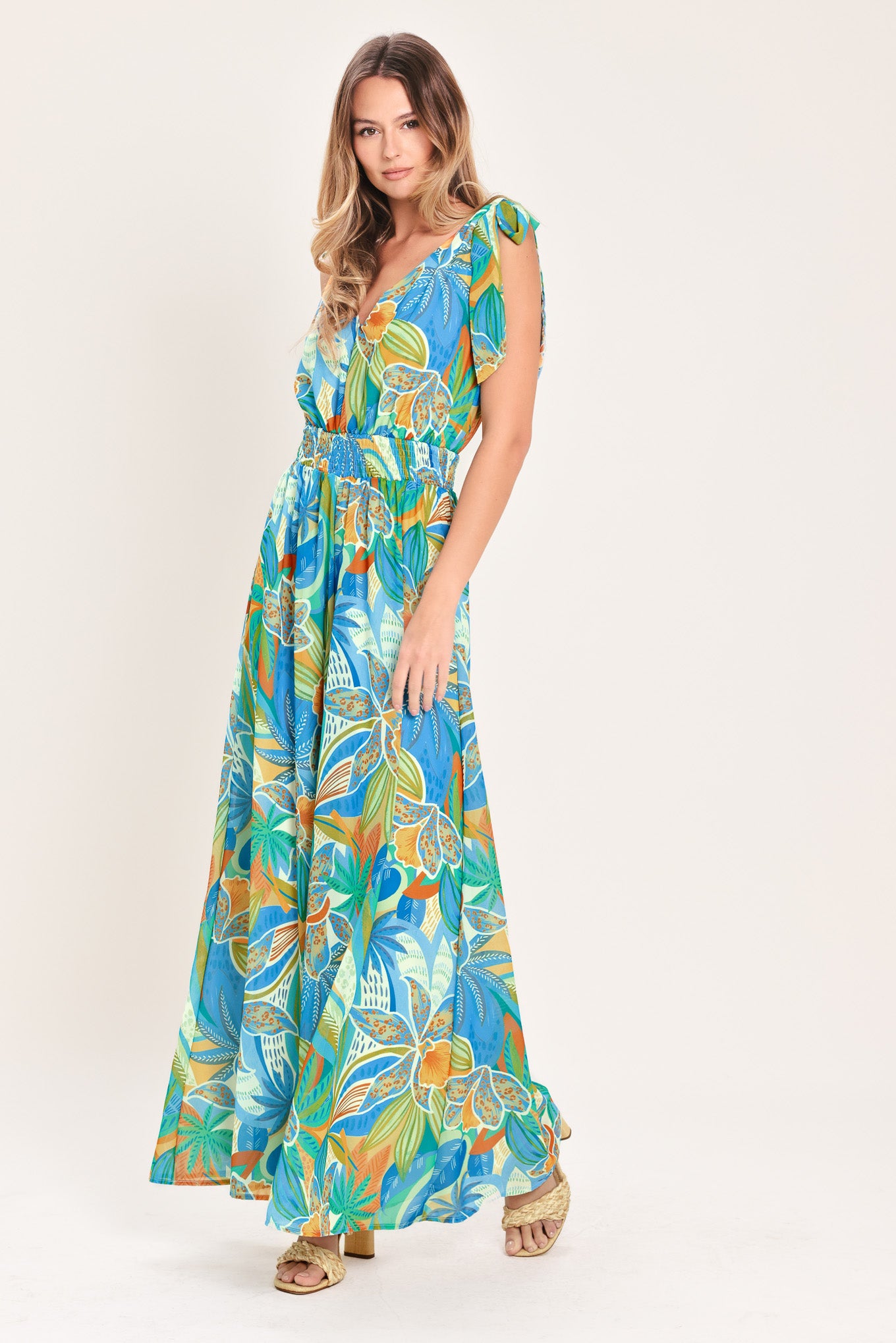 Woman wearing a blue multicolored patterned woven jumpsuit featuring V neckline, shoulder ties, smocked waistband and wide leg | Flying Tomato