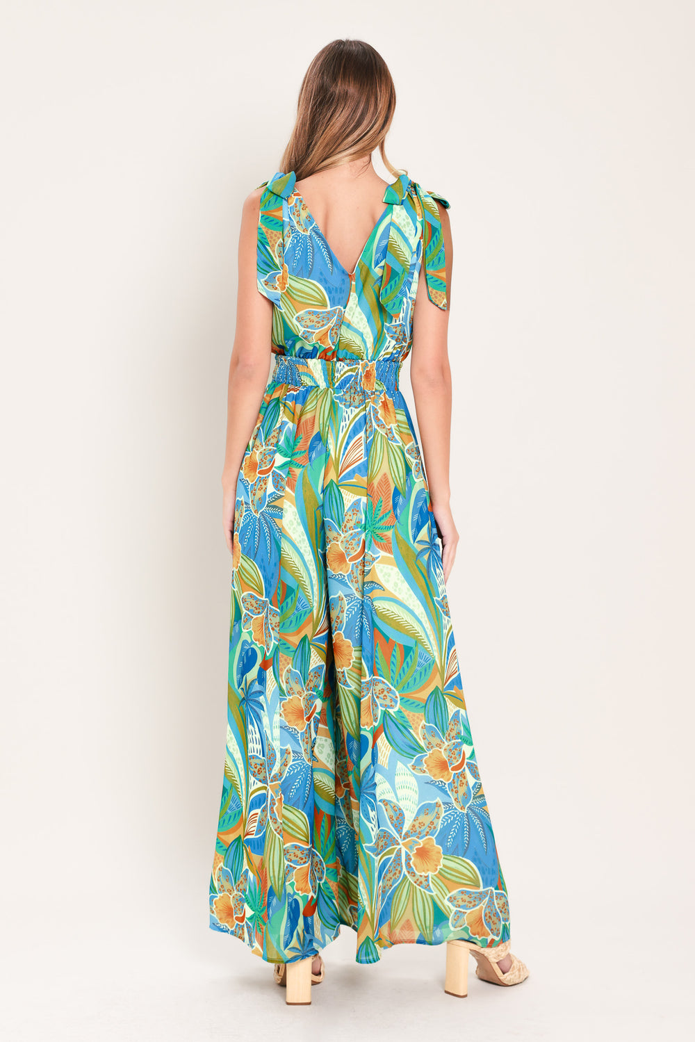 Woman wearing a blue multicolored patterned woven jumpsuit featuring V neckline, shoulder ties, smocked waistband and wide leg | Flying Tomato