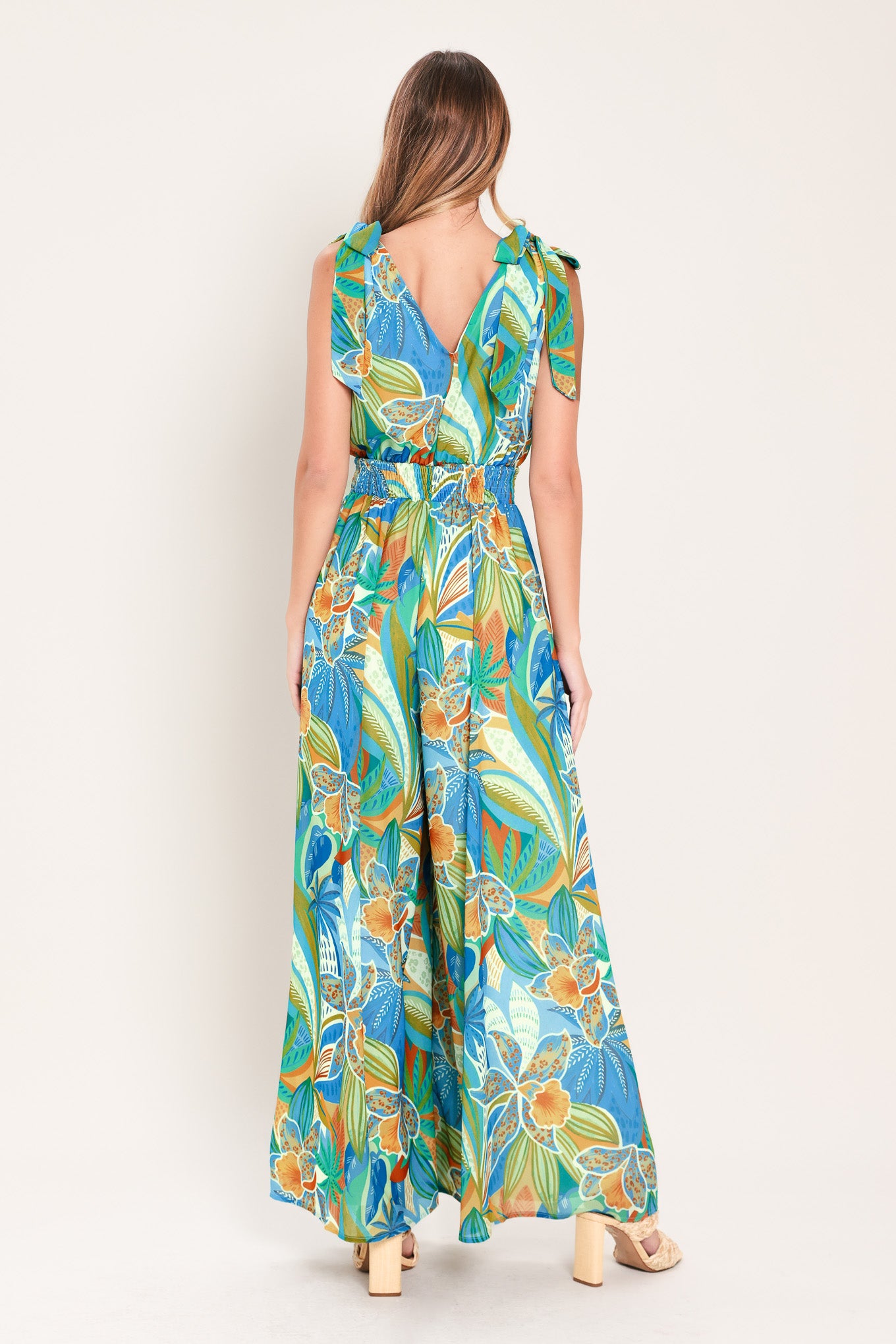 Woman wearing a blue multicolored patterned woven jumpsuit featuring V neckline, shoulder ties, smocked waistband and wide leg | Flying Tomato