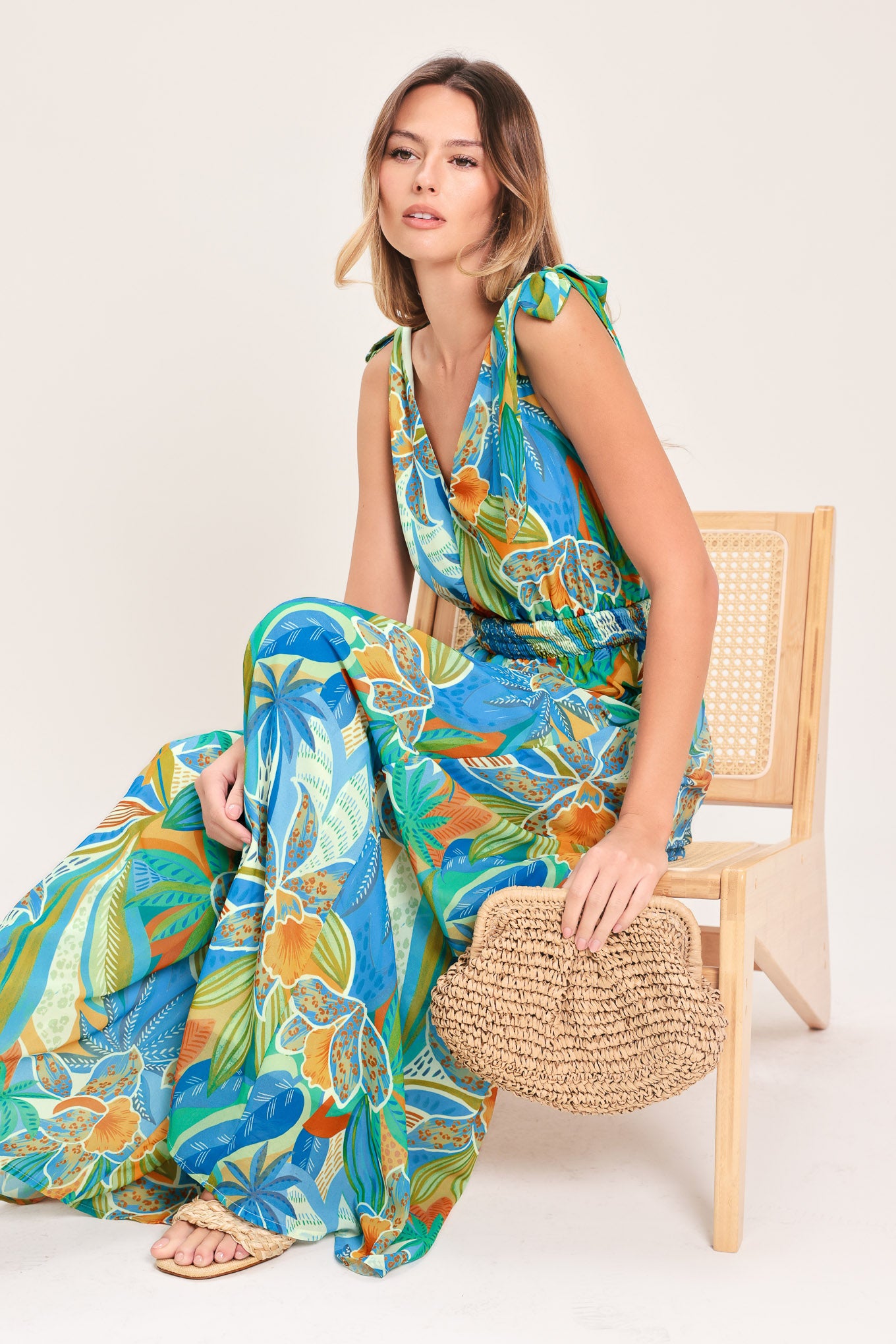 Woman wearing a blue multicolored patterned woven jumpsuit featuring V neckline, shoulder ties, smocked waistband and wide leg | Flying Tomato