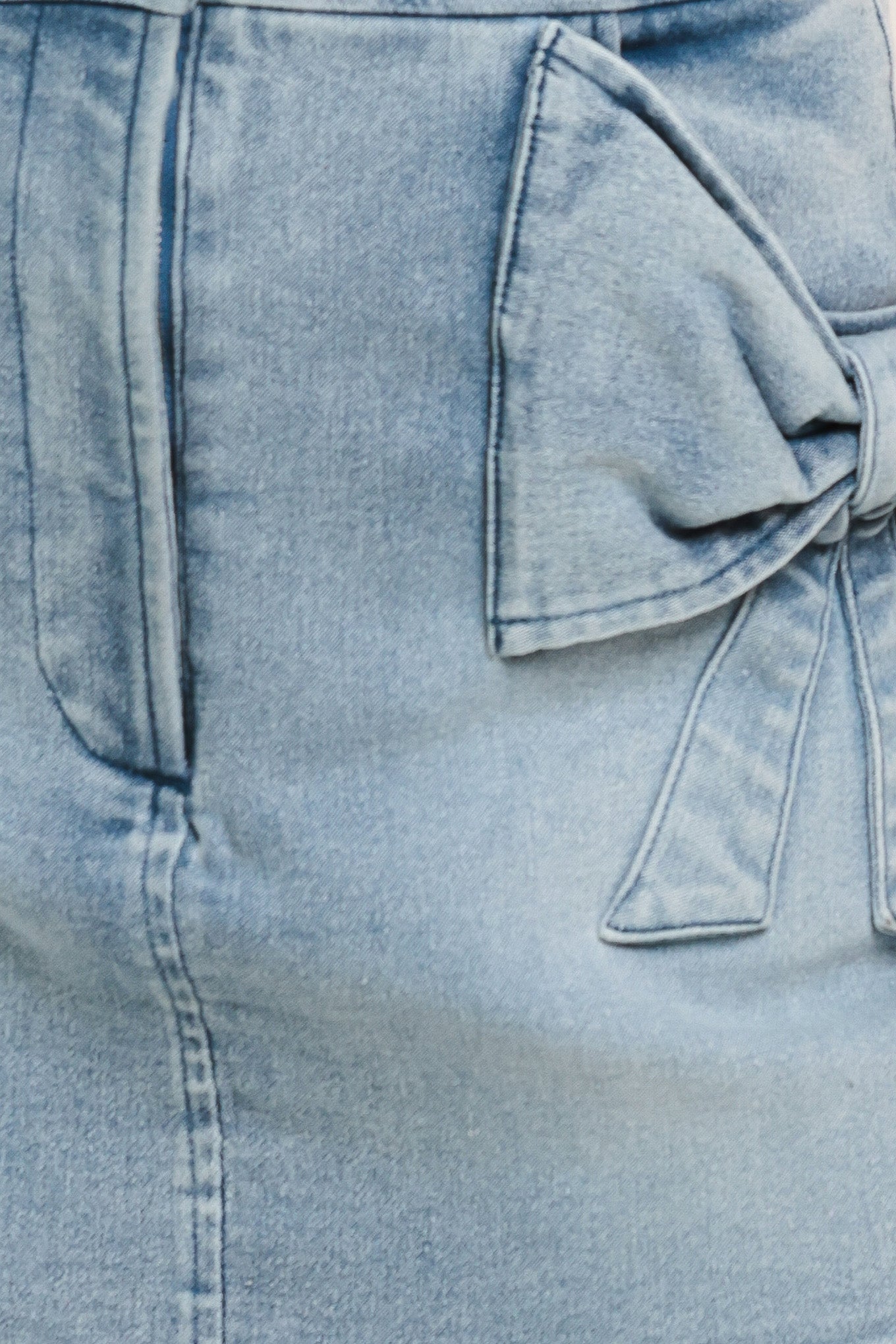 Close-up of a light blue denim skirt with a bow detail on pockets | Flying Tomato