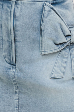 Close-up of a light blue denim skirt with a bow detail on pockets | Flying Tomato