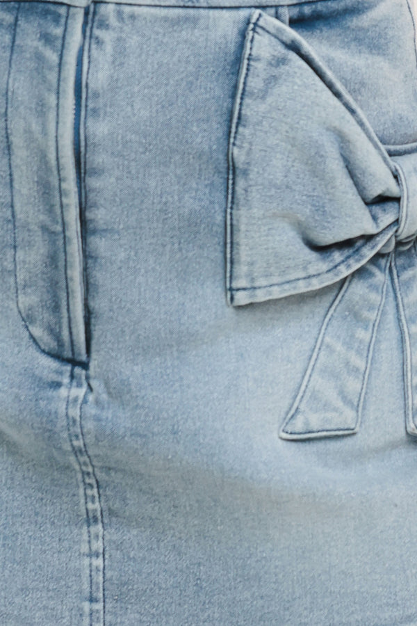 Close-up of a light blue denim skirt with a bow detail on pockets | Flying Tomato
