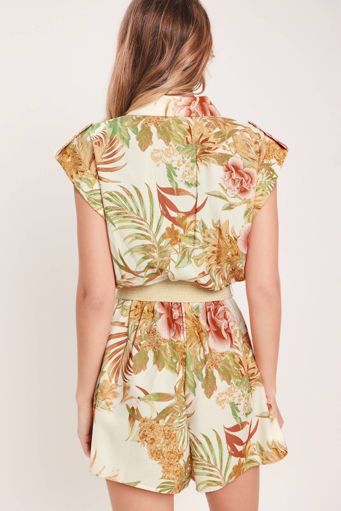 Woman wearing a floral romper featuring front button down, cuffed short sleeve with tab, elastic waist and contrasting belt | Flying Tomato