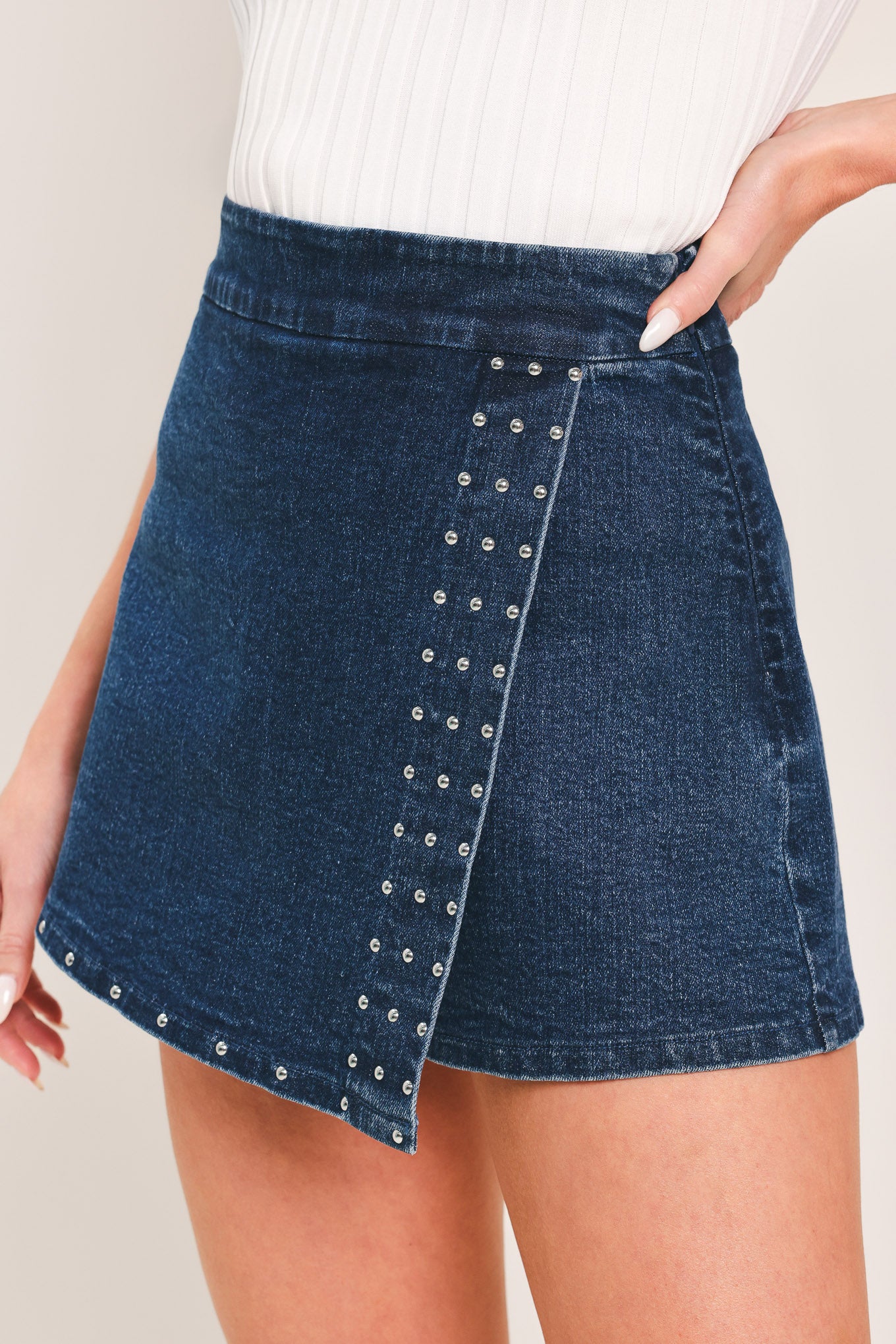 Woman wearing a blue denim skort featuring stud embellished front flap and side zipper closure | Flying Tomato