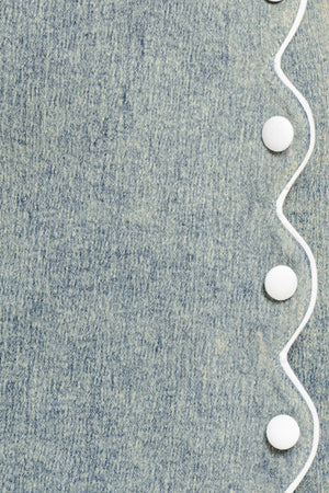 Close-up of denim fabric with a white scallop details and buttons | Flying Tomato