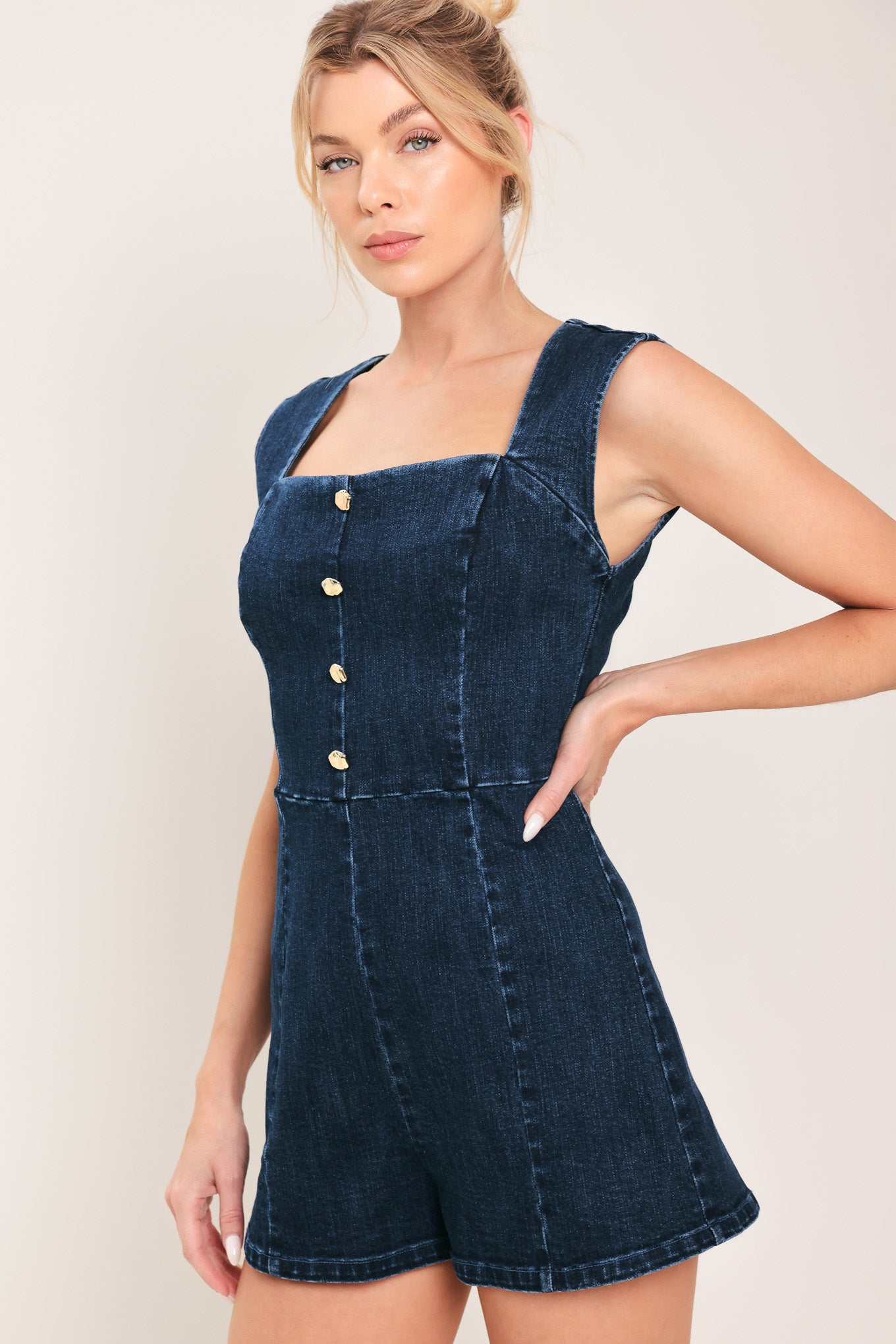 Woman wearing a denim romper featuring square neckline, sleeveless, front button detail and back zipper closure | Flying Tomato