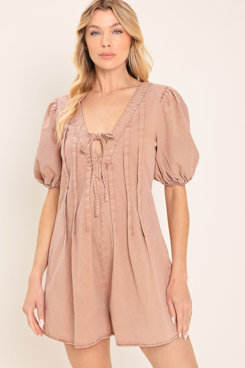 Woman wearing a light peach toned romper with puff sleeves and v-cut with bows | Flying Tomato
