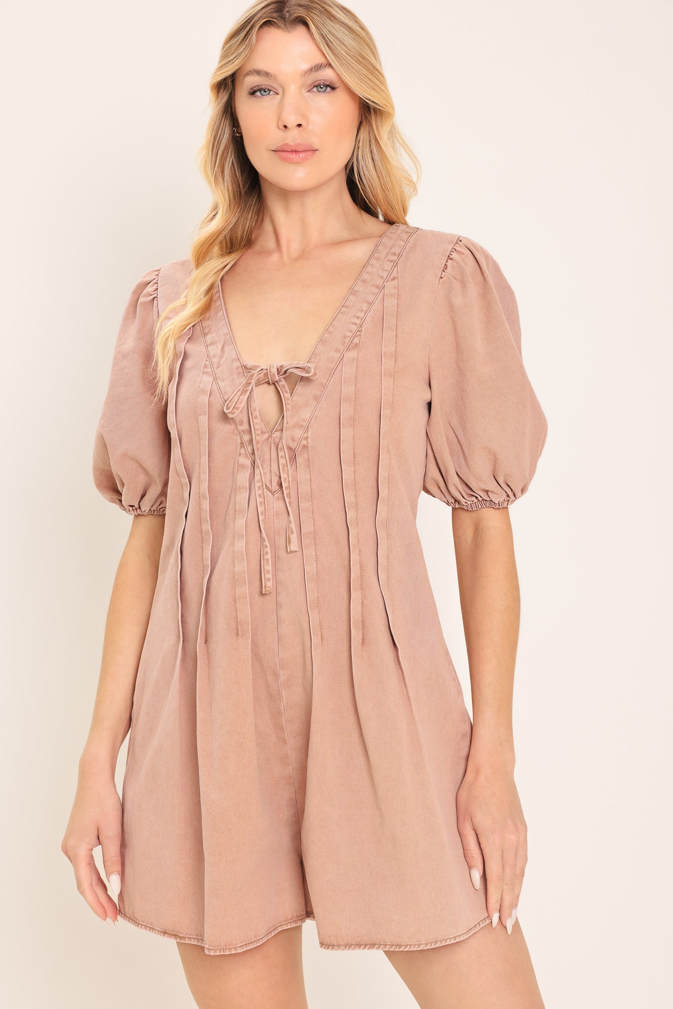 Woman wearing a light peach toned romper with puff sleeves and v-cut with bows | Flying Tomato