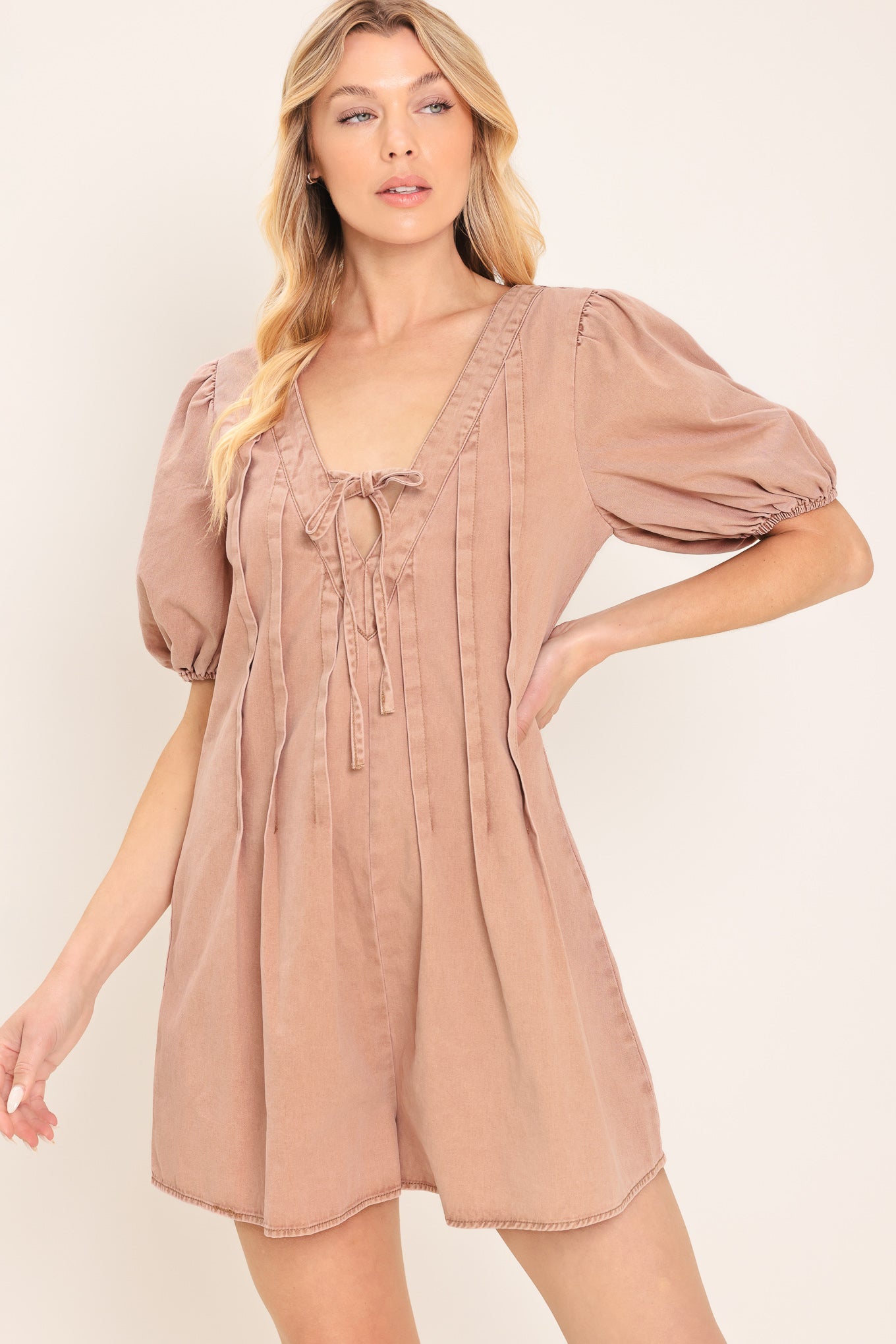 Woman wearing a light peach toned romper with puff sleeves and v-cut with bows | Flying Tomato