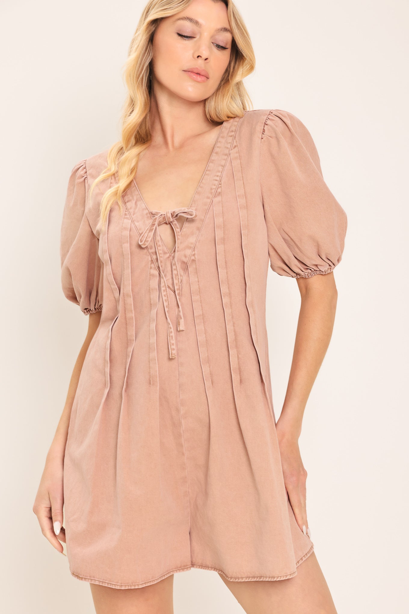 Woman wearing a light peach toned romper with puff sleeves and v-cut with bows | Flying Tomato