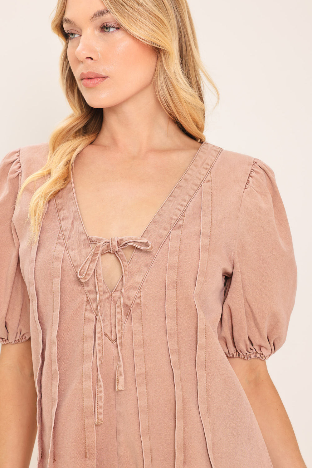 Woman wearing a light peach toned romper with puff sleeves and v-cut with bows | Flying Tomato
