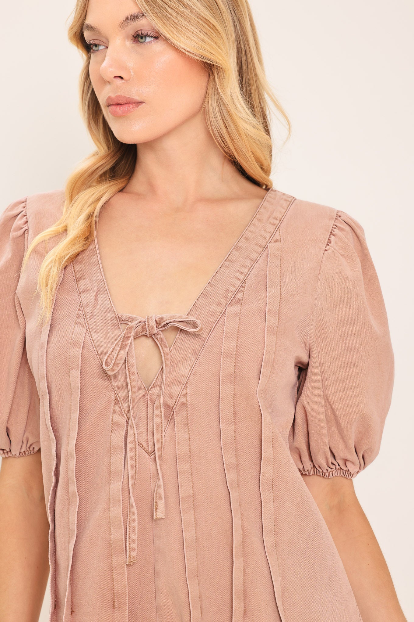Woman wearing a light peach toned romper with puff sleeves and v-cut with bows | Flying Tomato