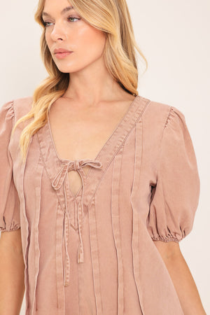 Woman wearing a light peach toned romper with puff sleeves and v-cut with bows | Flying Tomato