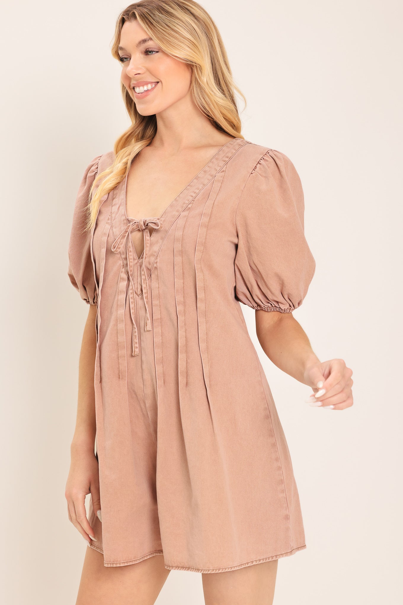 Woman wearing a light peach toned romper with puff sleeves and v-cut with bows | Flying Tomato