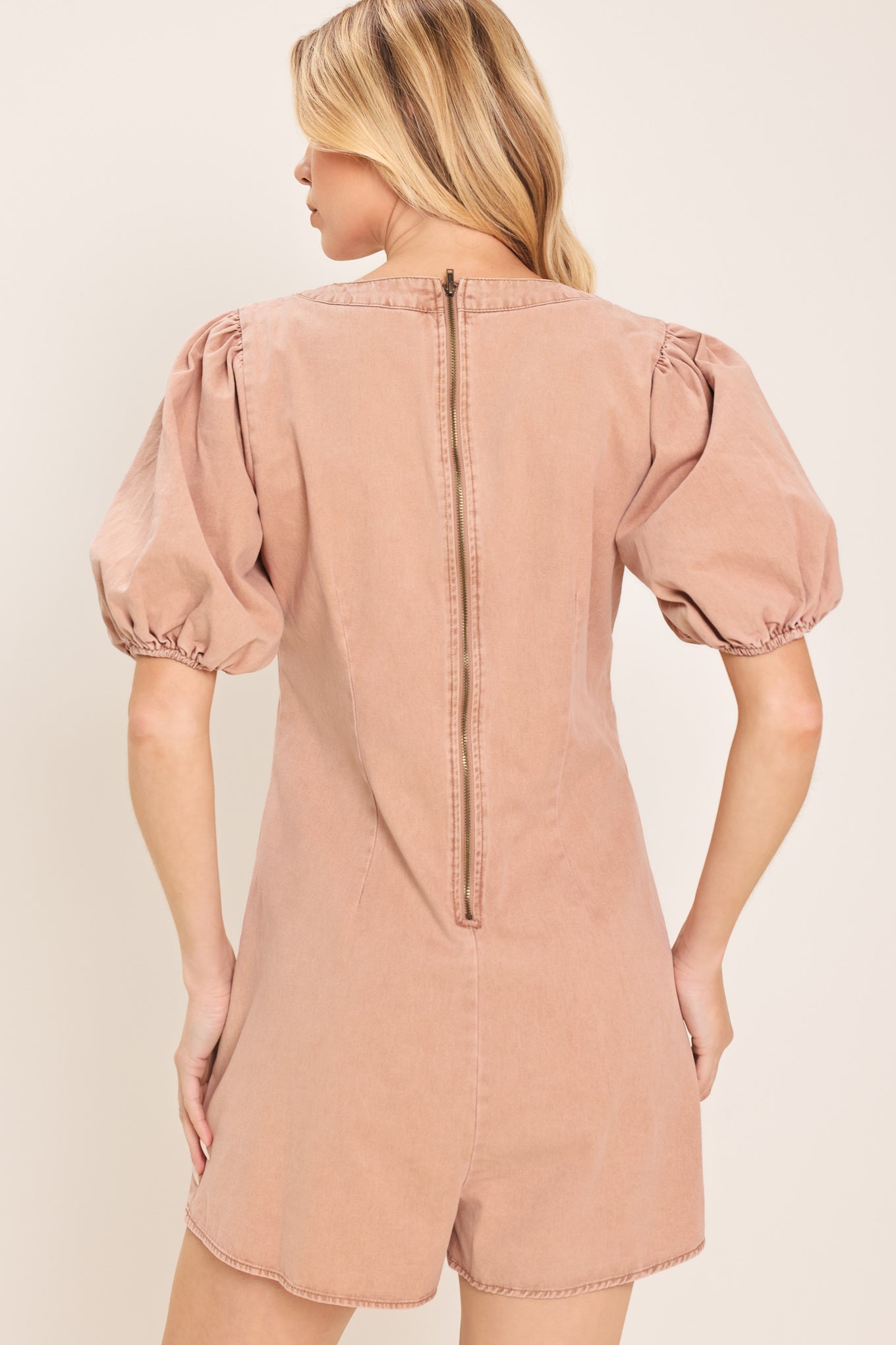 Woman wearing a light peach toned romper with puff sleeves and v-cut with bows | Flying Tomato