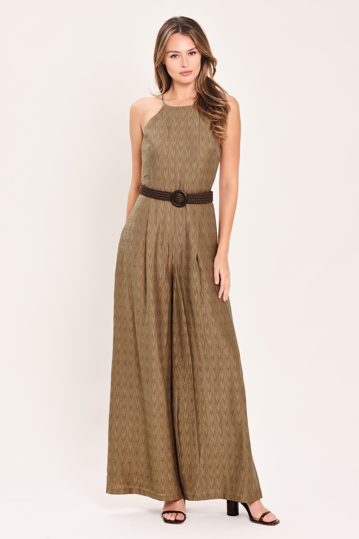 A woman modeling a sleeveless, high-neck, wide-leg jumpsuit in a textured brown fabric with a dark brown belt | Flying Tomato
