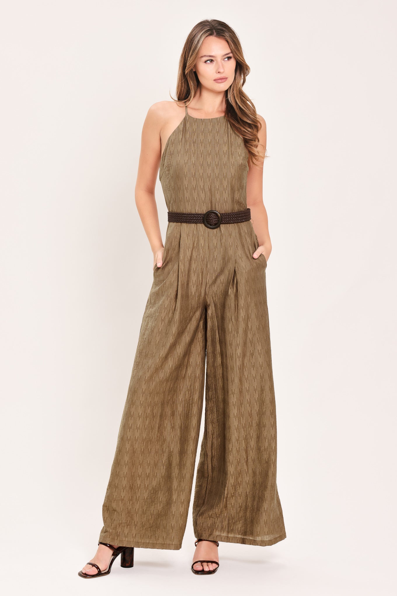 A woman modeling a sleeveless, high-neck, wide-leg jumpsuit in a textured brown fabric with a dark brown belt | Flying Tomato