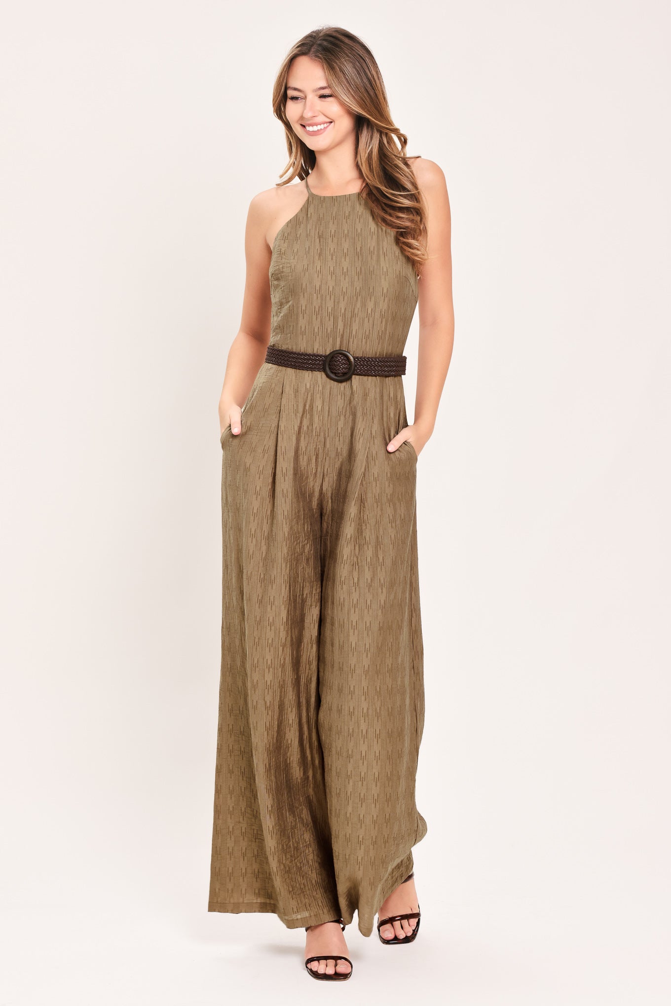 A woman modeling a sleeveless, high-neck, wide-leg jumpsuit in a textured brown fabric with a dark brown belt | Flying Tomato