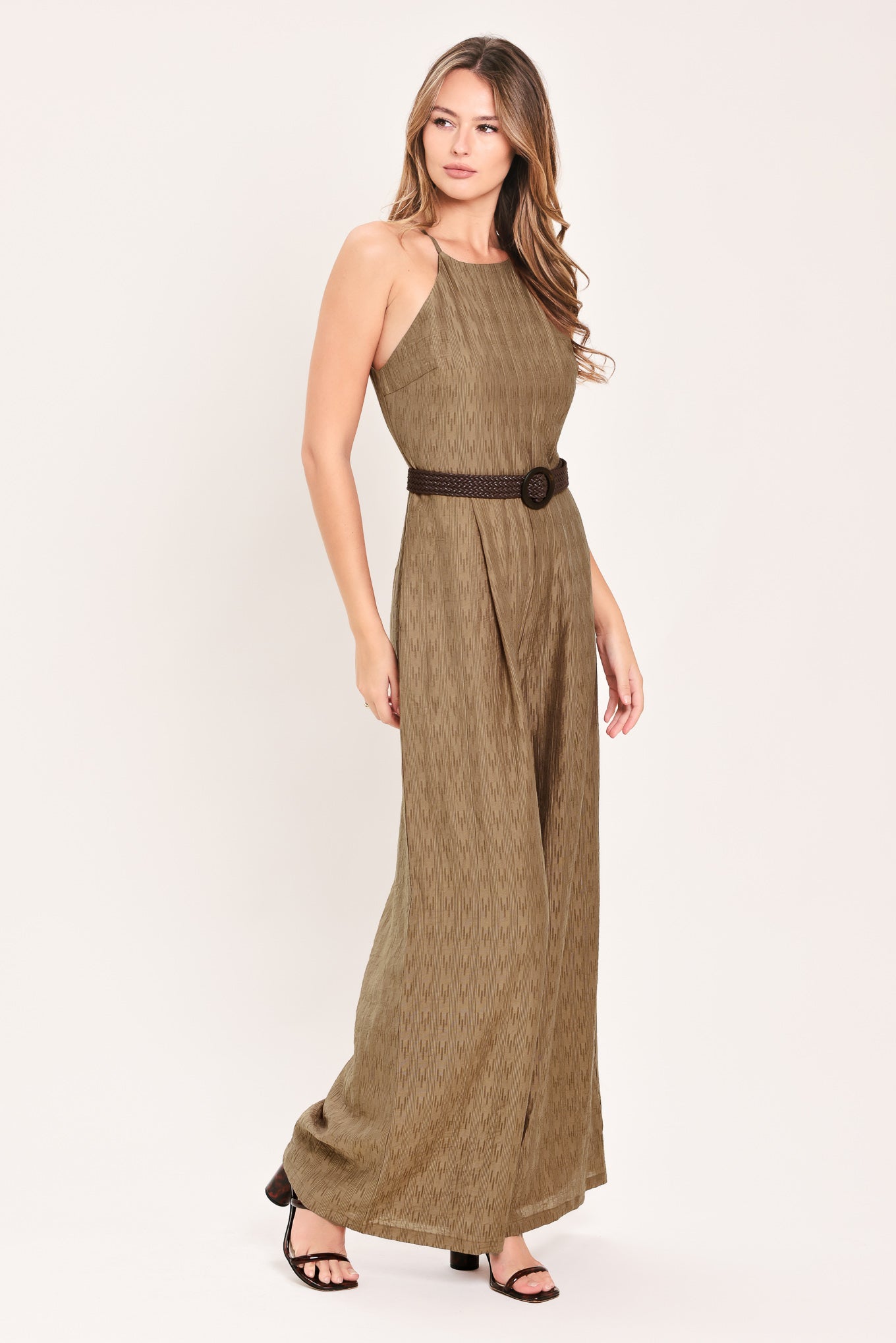 A woman modeling a sleeveless, high-neck, wide-leg jumpsuit in a textured brown fabric with a dark brown belt | Flying Tomato