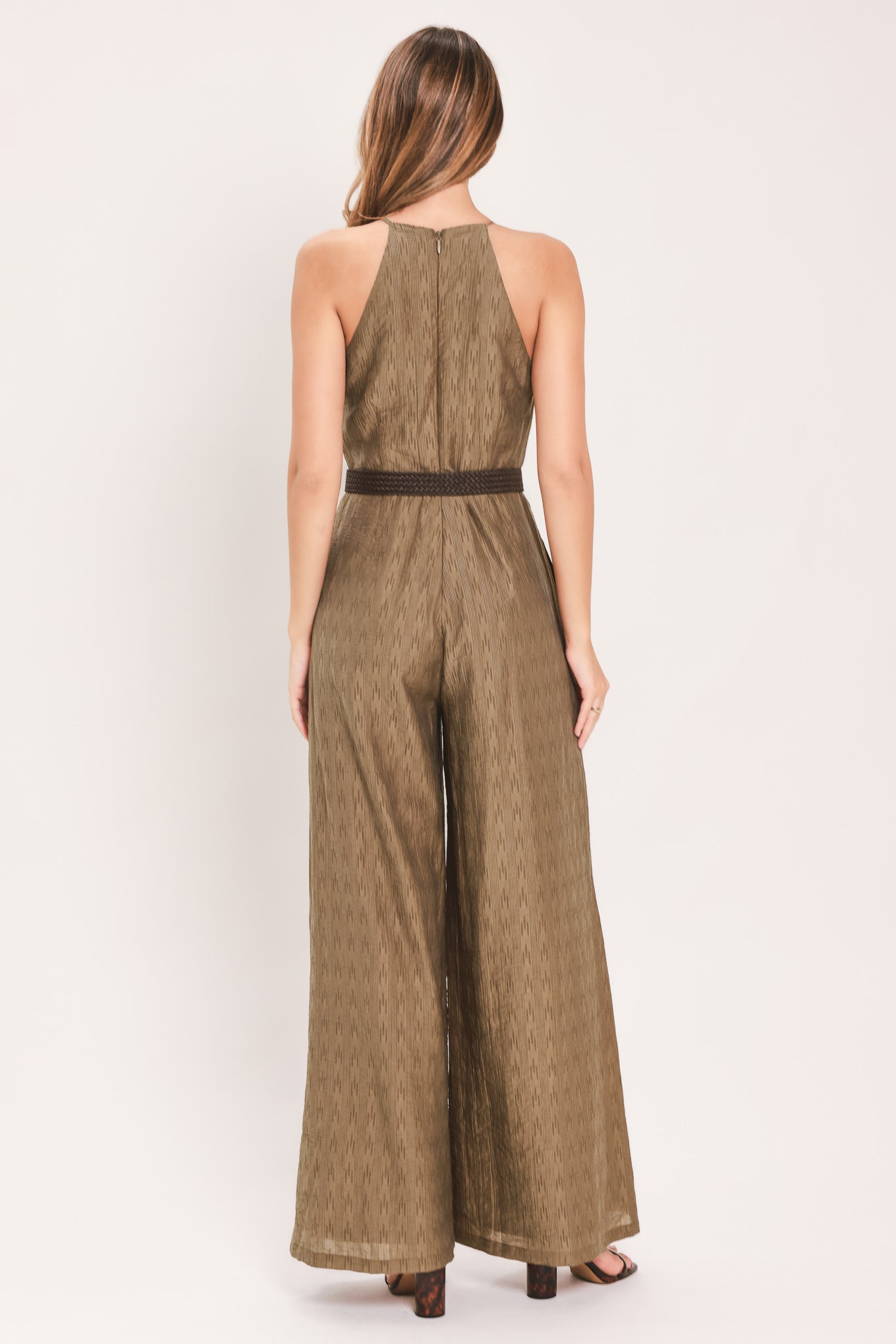 A woman modeling a sleeveless, high-neck, wide-leg jumpsuit in a textured brown fabric with a dark brown belt | Flying Tomato