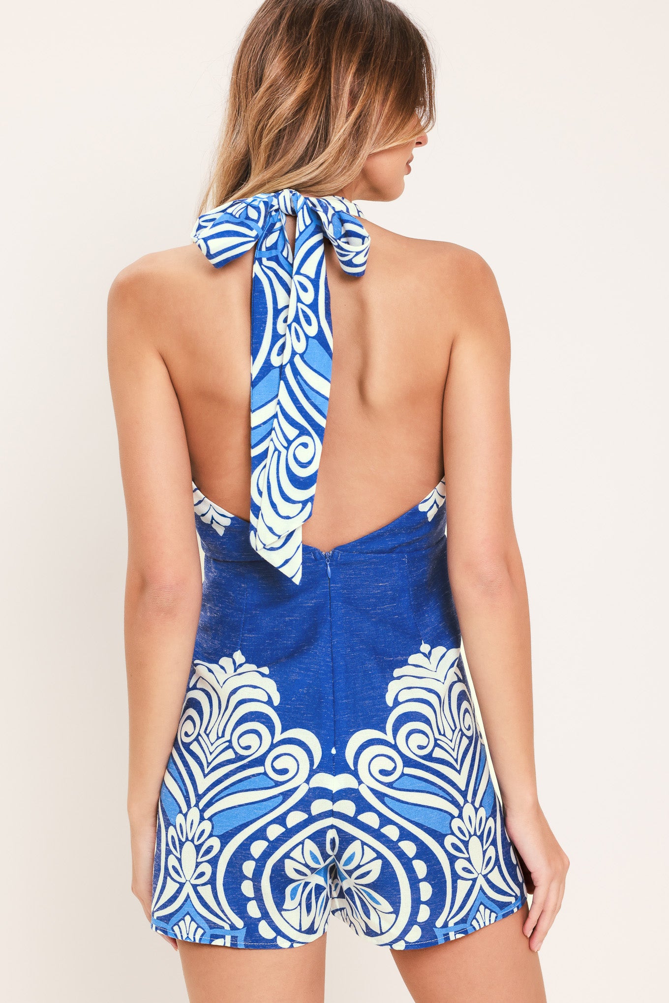 Woman wearing a blue and white patterned woven skort romper featuring halter v-neckline with back tie and bare back with zipper closure | Flying Tomato