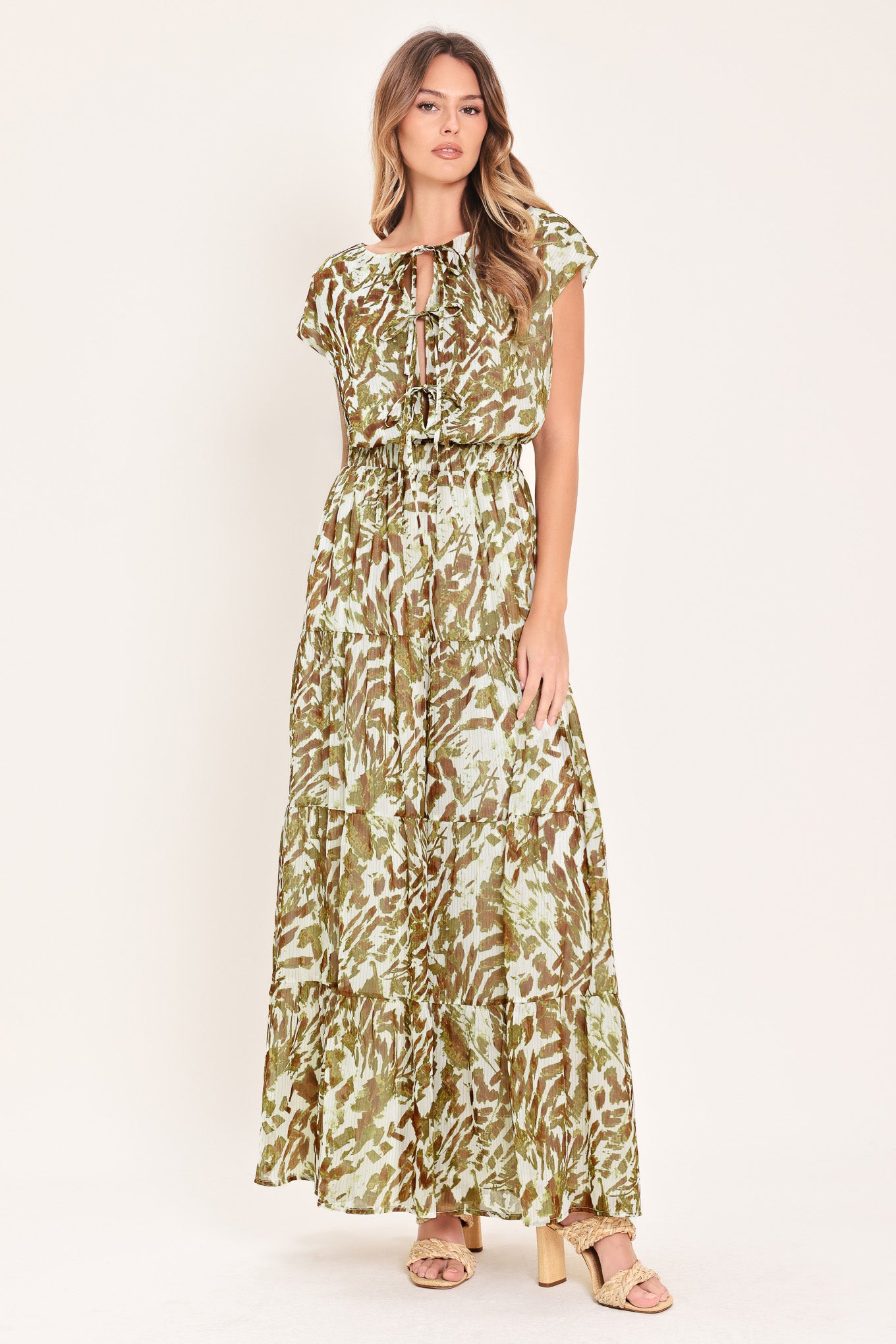 Woman wearing an olive green, brown, and white patterned woven jumpsuit featuring round neckline, short sleeve, front tie detail, elastic waist and tier wide leg pant | Flying Tomato