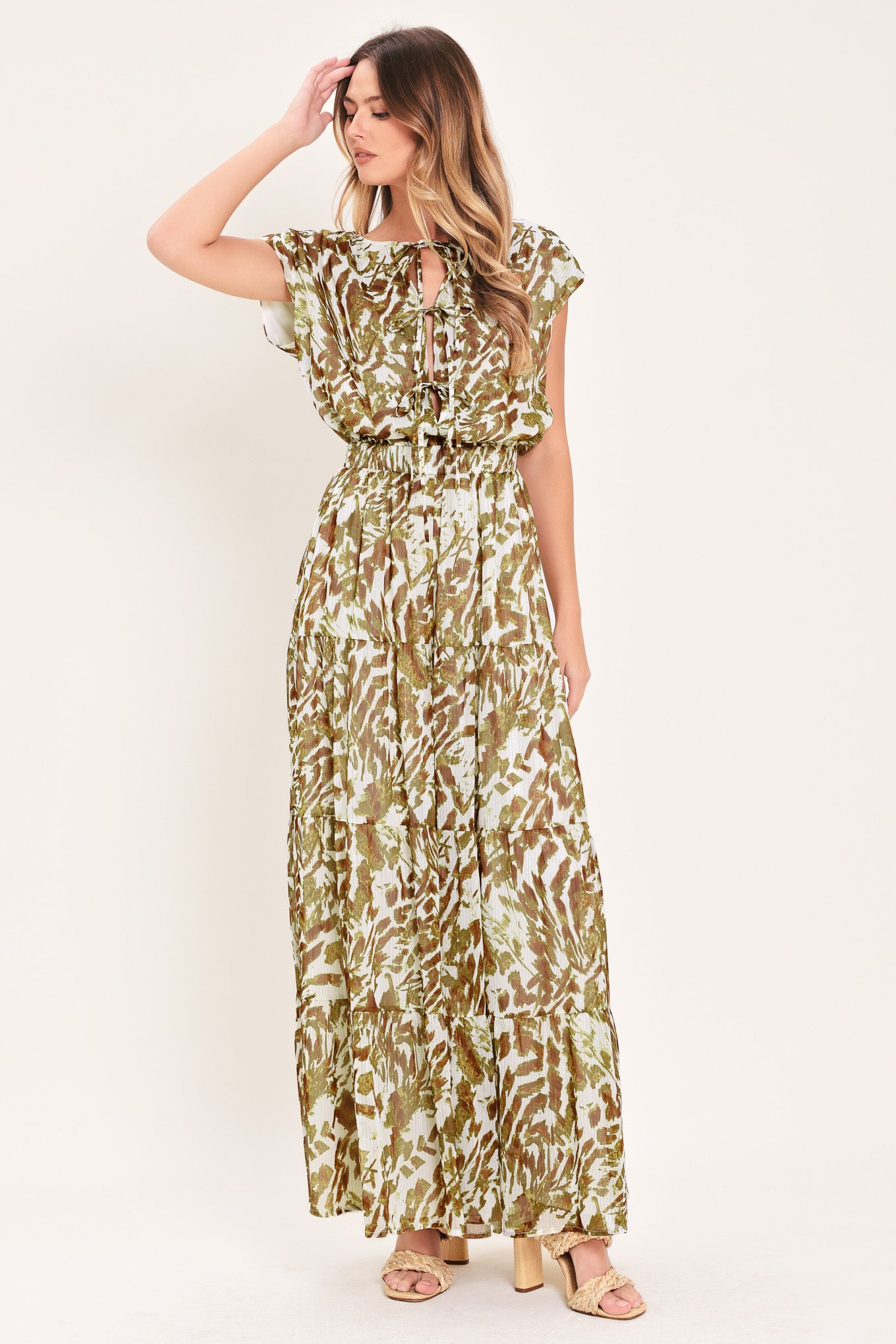Woman wearing an olive green, brown, and white patterned woven jumpsuit featuring round neckline, short sleeve, front tie detail, elastic waist and tier wide leg pant | Flying Tomato