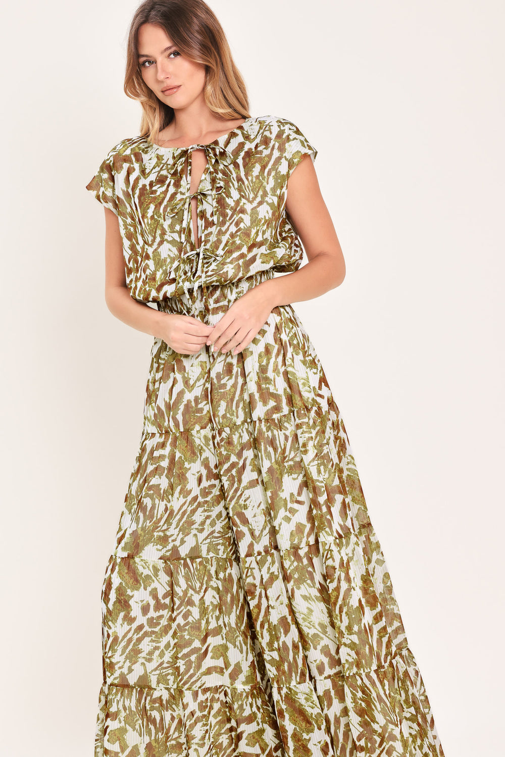 Woman wearing an olive green, brown, and white patterned woven jumpsuit featuring round neckline, short sleeve, front tie detail, elastic waist and tier wide leg pant | Flying Tomato
