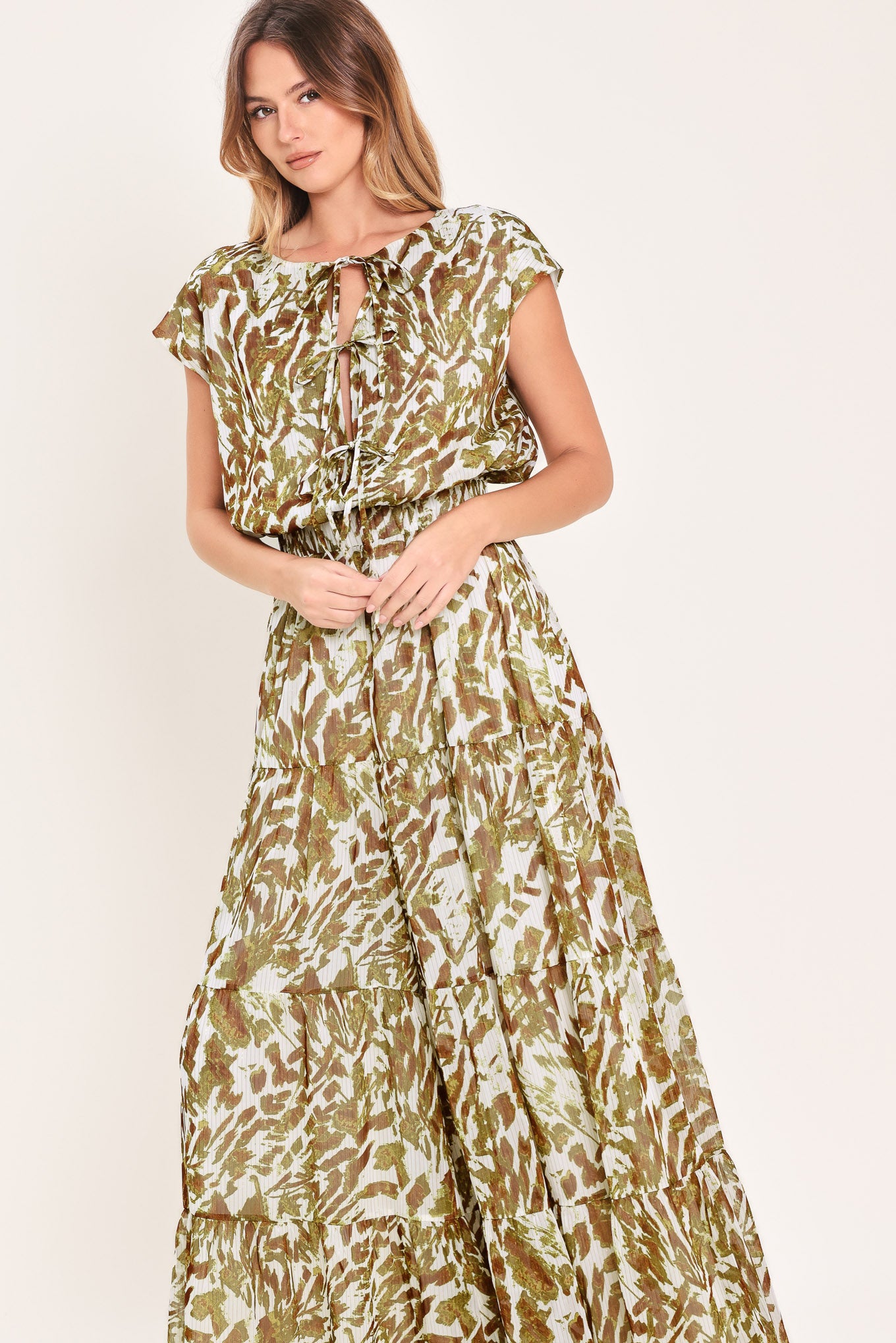 Woman wearing an olive green, brown, and white patterned woven jumpsuit featuring round neckline, short sleeve, front tie detail, elastic waist and tier wide leg pant | Flying Tomato