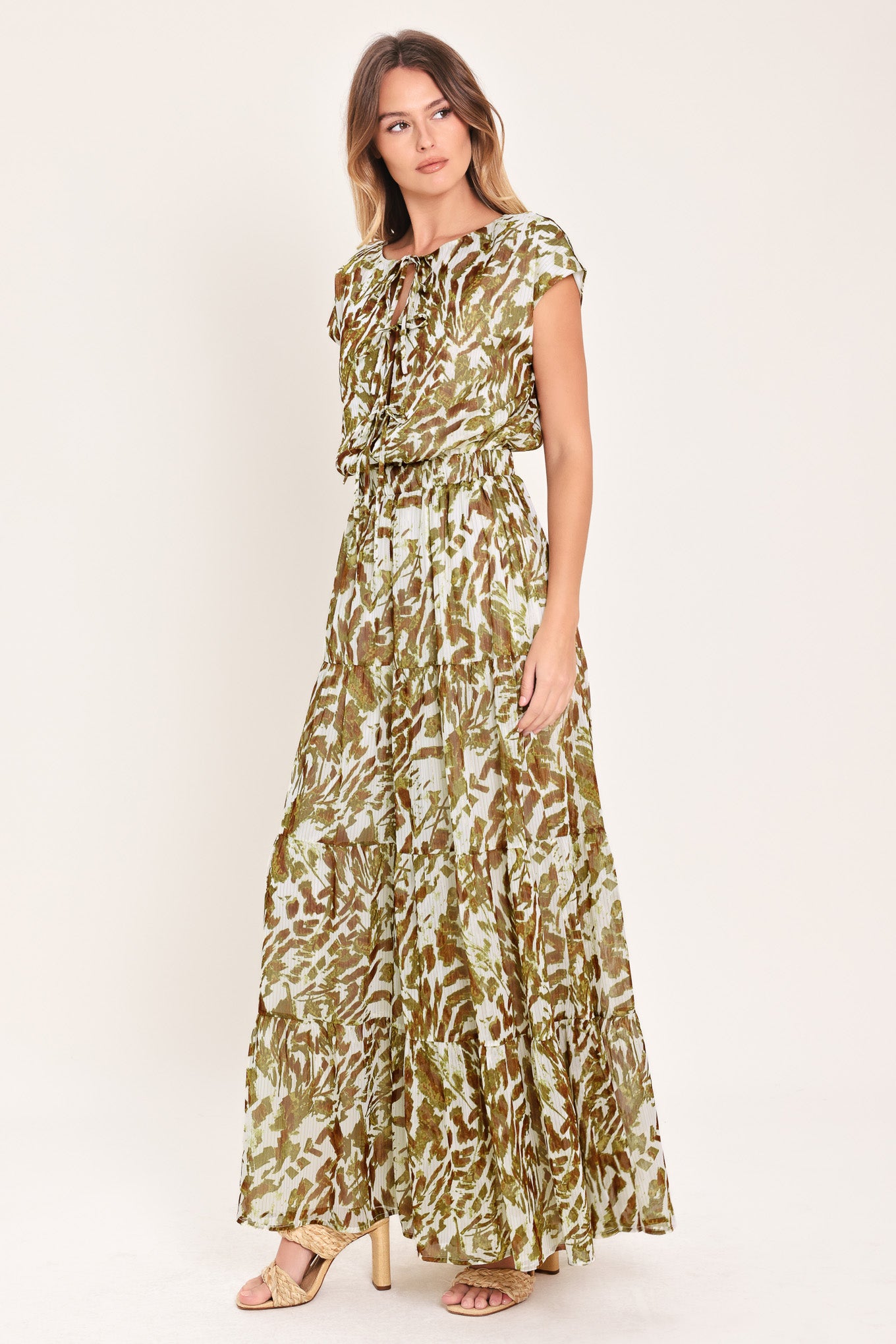 Woman wearing an olive green, brown, and white patterned woven jumpsuit featuring round neckline, short sleeve, front tie detail, elastic waist and tier wide leg pant | Flying Tomato