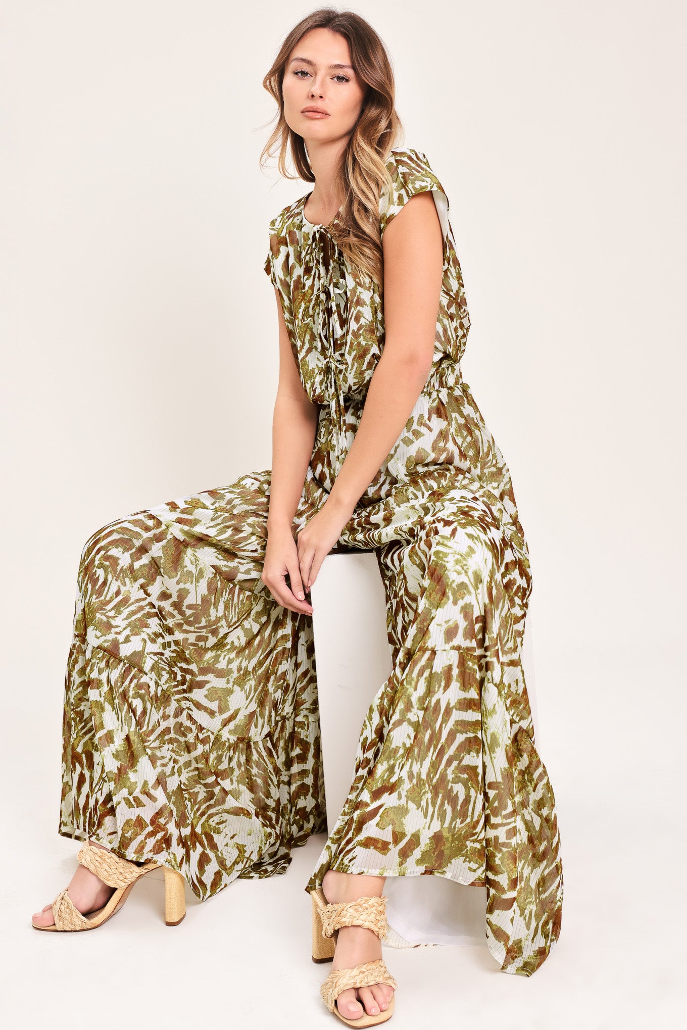 Woman wearing an olive green, brown, and white patterned woven jumpsuit featuring round neckline, short sleeve, front tie detail, elastic waist and tier wide leg pant | Flying Tomato